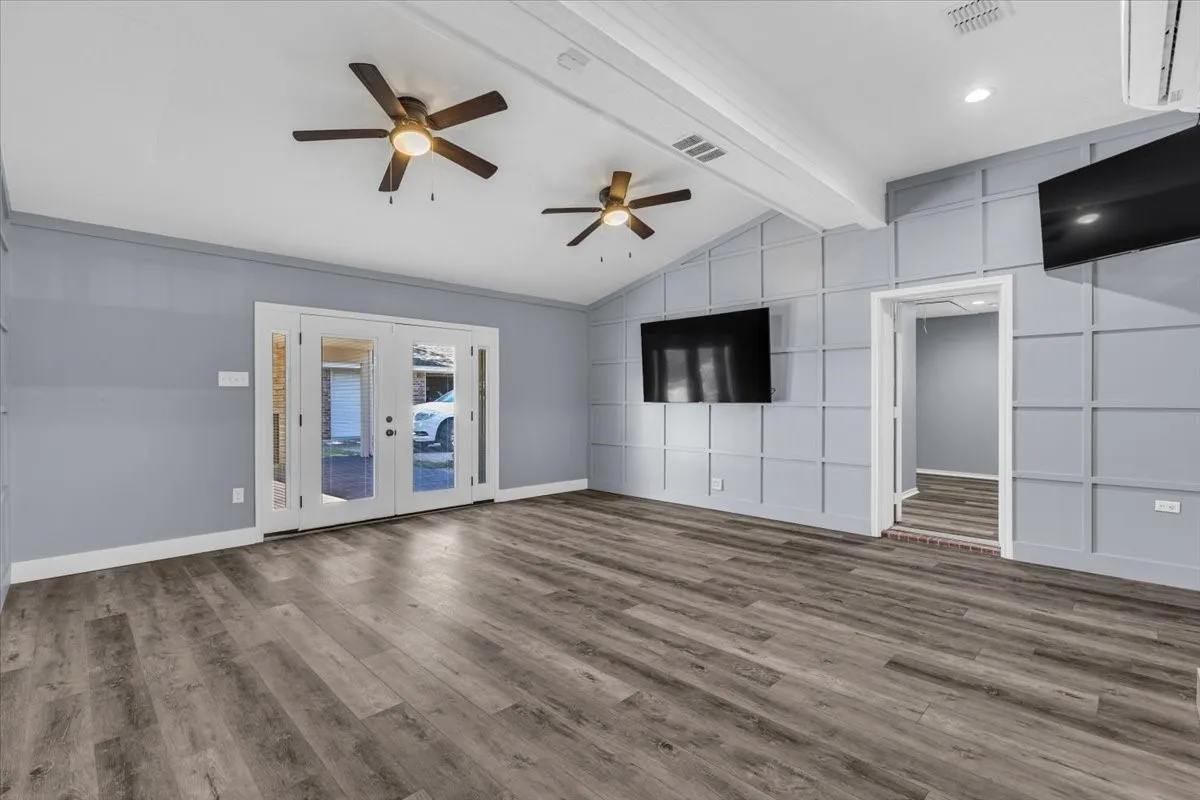 This versatile, expansive room is perfect as a game room, living area, or flexible space to suit your needs, featuring vaulted ceilings, stylish accent wall paneling, dual ceiling fans, and elegant French doors that open to the exterior.