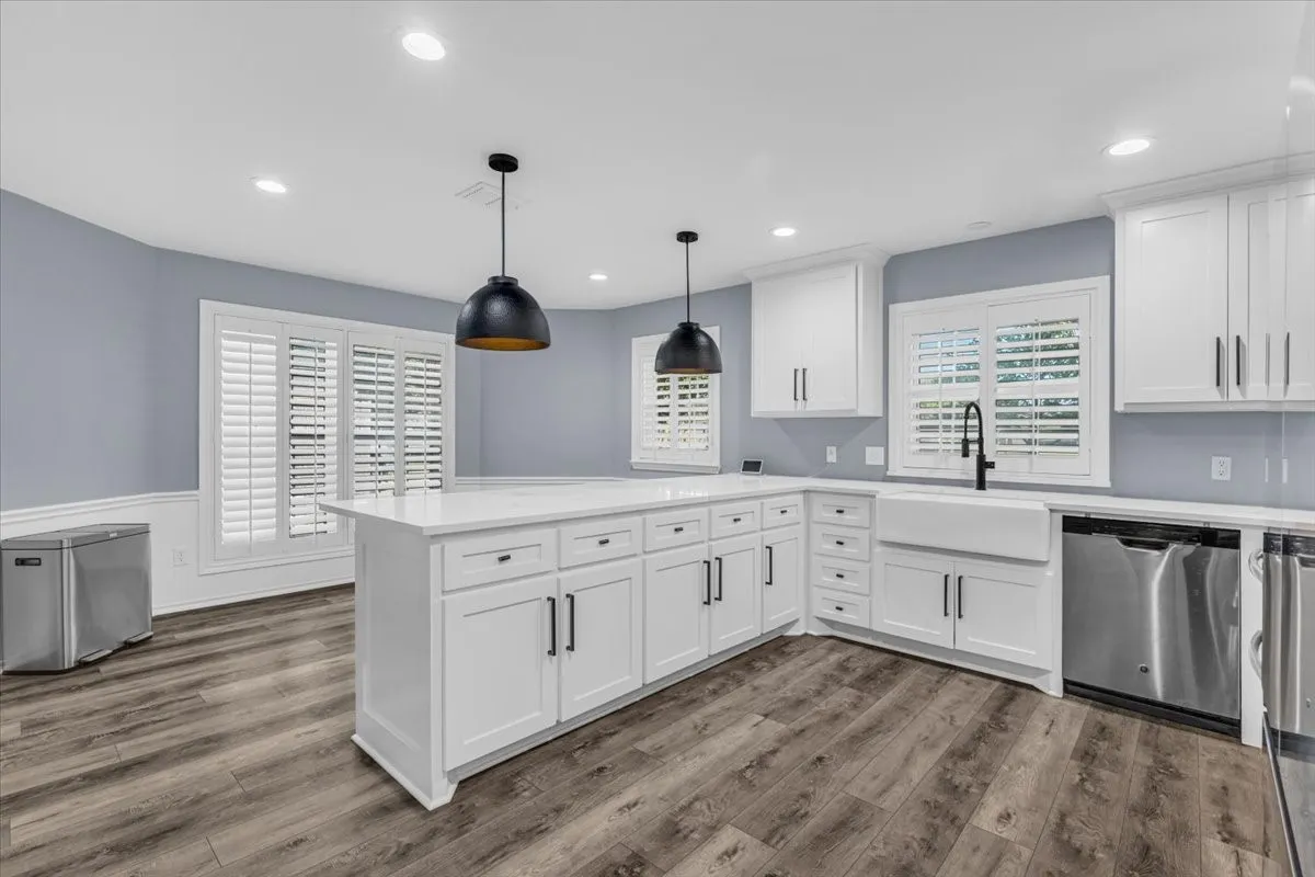 The completely updated kitchen is a chef's dream, featuring crisp white cabinetry, generous quartz counter space, a classic farmhouse sink, striking modern pendant lighting, and stainless steel appliances.