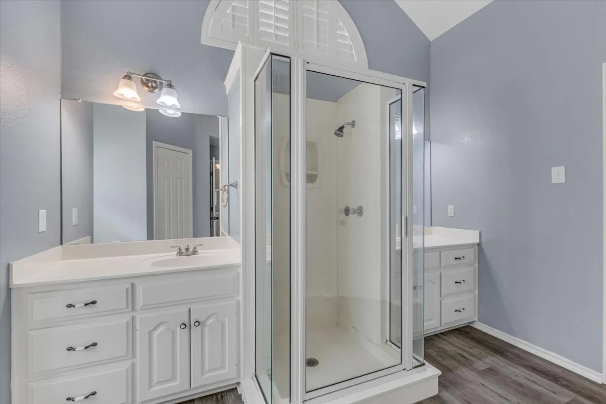 This functional  second primary bathroom features dual vanity areas, a convenient central walk-in shower, and vaulted ceilings that enhance the overall sense of space and light.