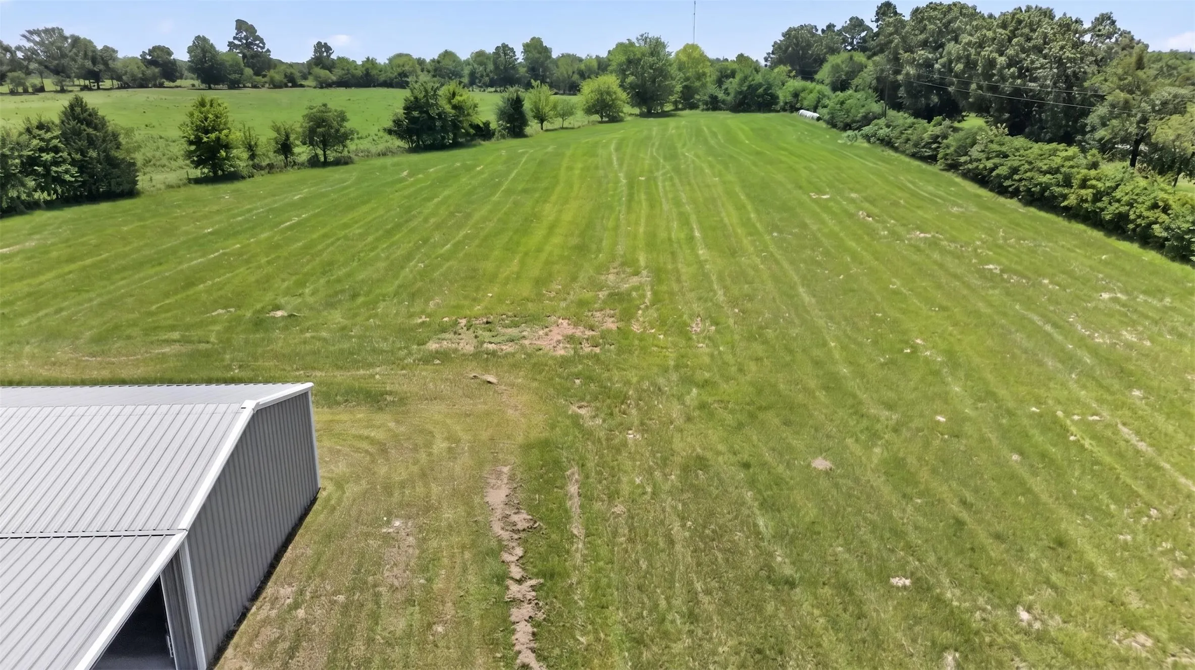 Expansive green land featuring a metal-sided building with a corrugated metal roof