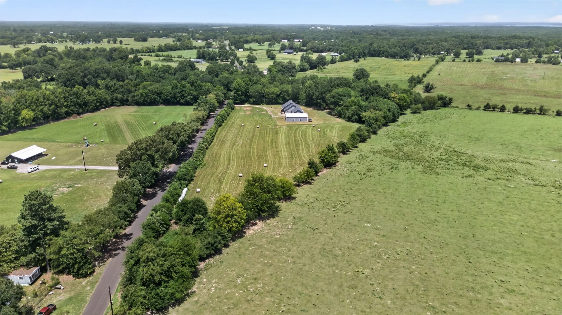 Expansive acreage featuring a modern barn structure, paved road access, multiple agricultural fields, and natural tree lines
