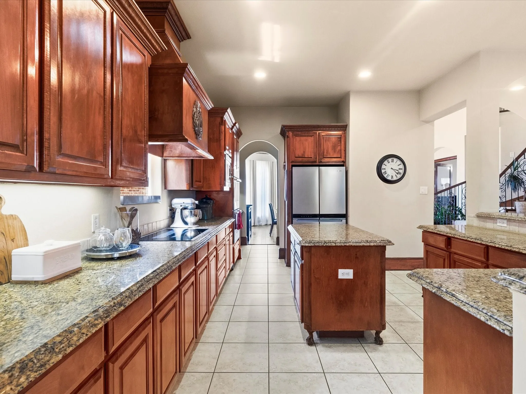 Spacious kitchen featuring extensive wood cabinetry, granite countertops, tile flooring, a central island, and stainless steel appliances