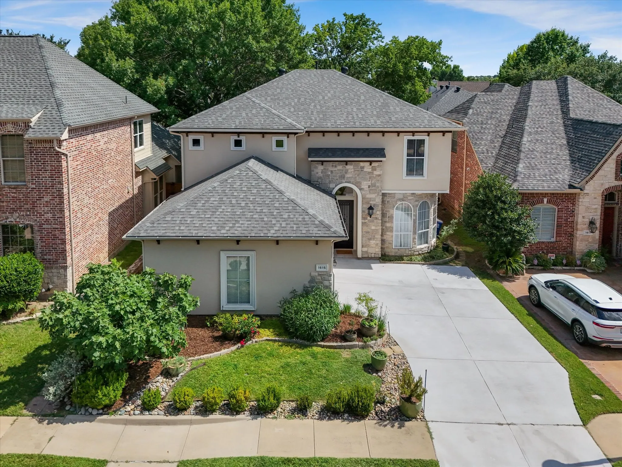 Two-story residence featuring a stucco and stone facade, arched window details, and a concrete driveway