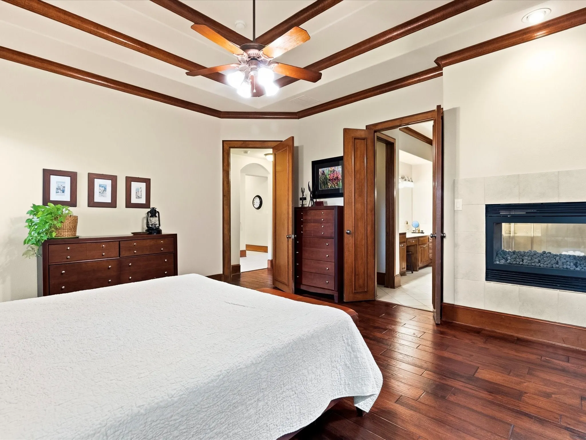 Bedroom featuring a built-in, double-sided fireplace, a tray ceiling with wood beam accents, a ceiling fan, and