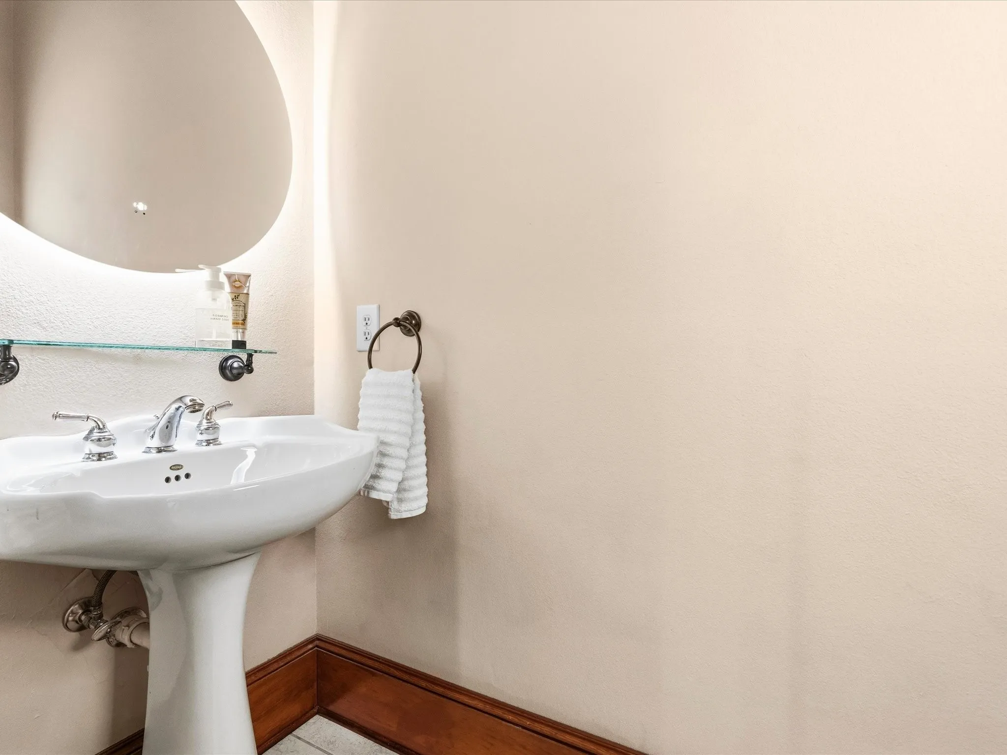 Half Bath with pedestal sink with chrome faucet, circular mirror, and glass shelf
