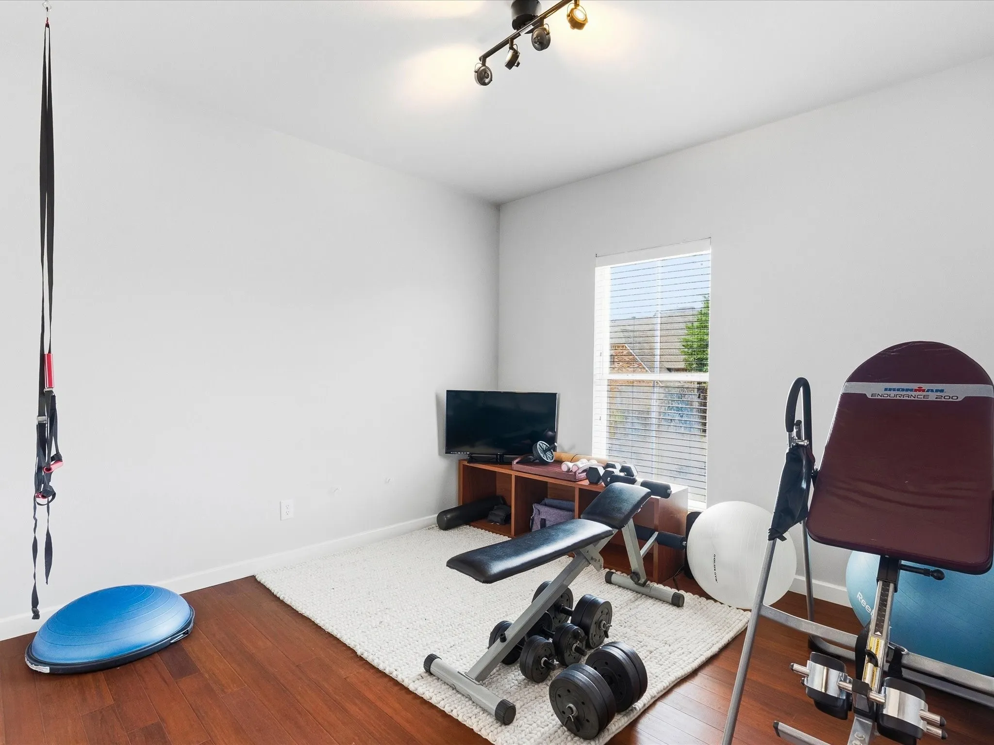 Bright Bedroom featuring wood-finish flooring, white walls, and a window with horizontal blinds