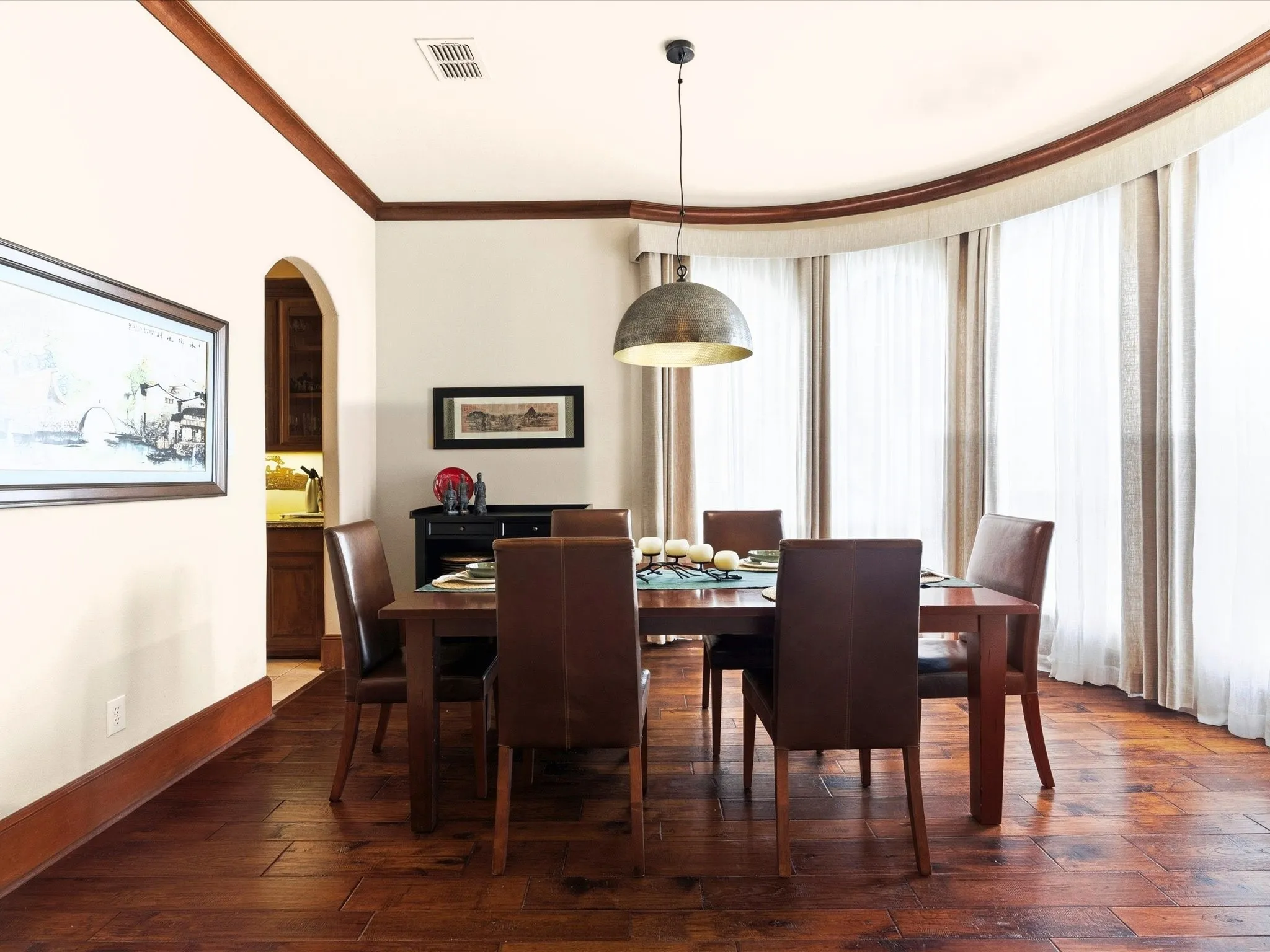 Elegant Dining room featuring wood-finish flooring, a contemporary pendant light fixture, and arched window treatments