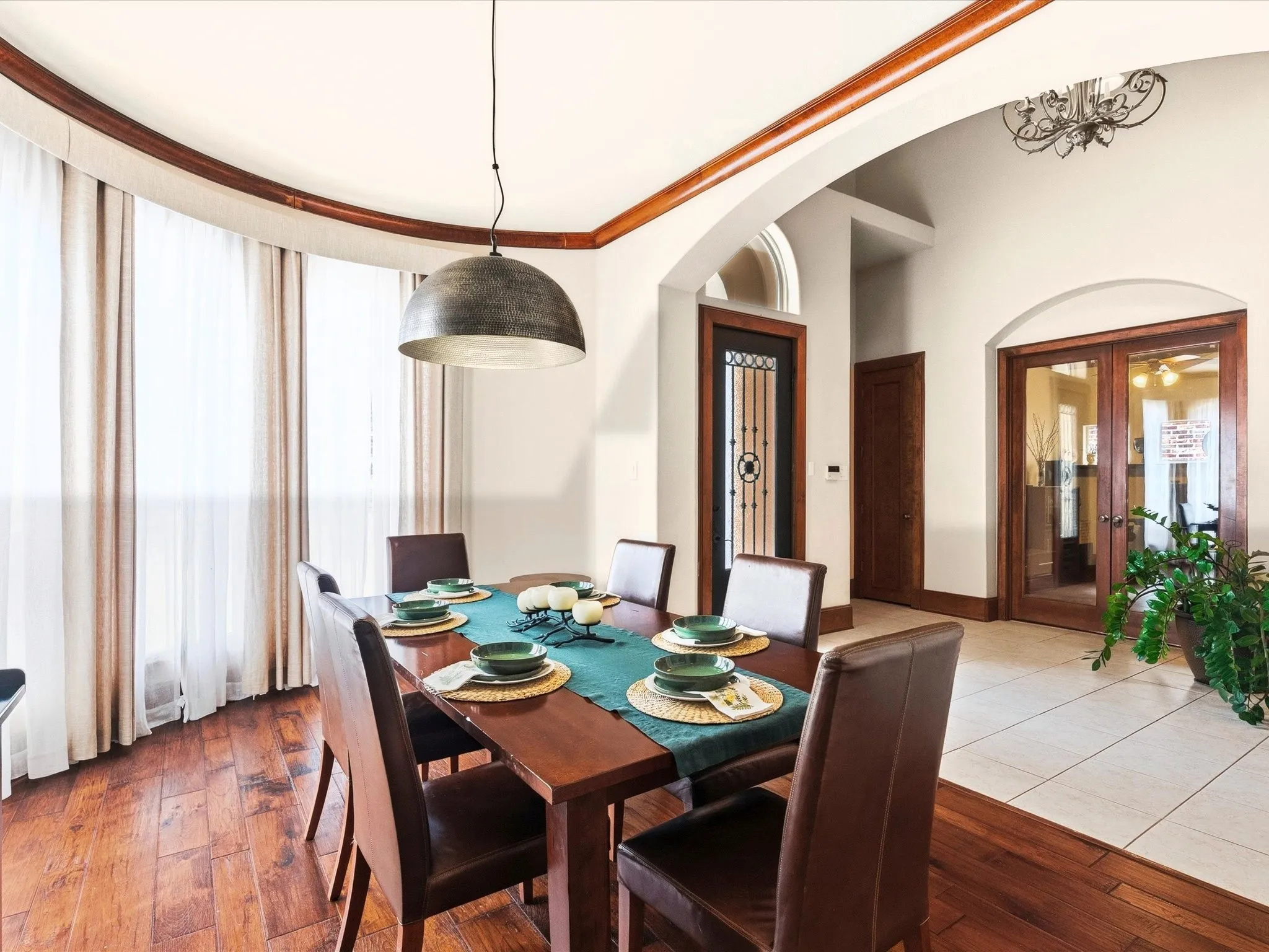 Dining area featuring wood-finish flooring, a contemporary dome pendant light, and a curved window wall with sheer drapes