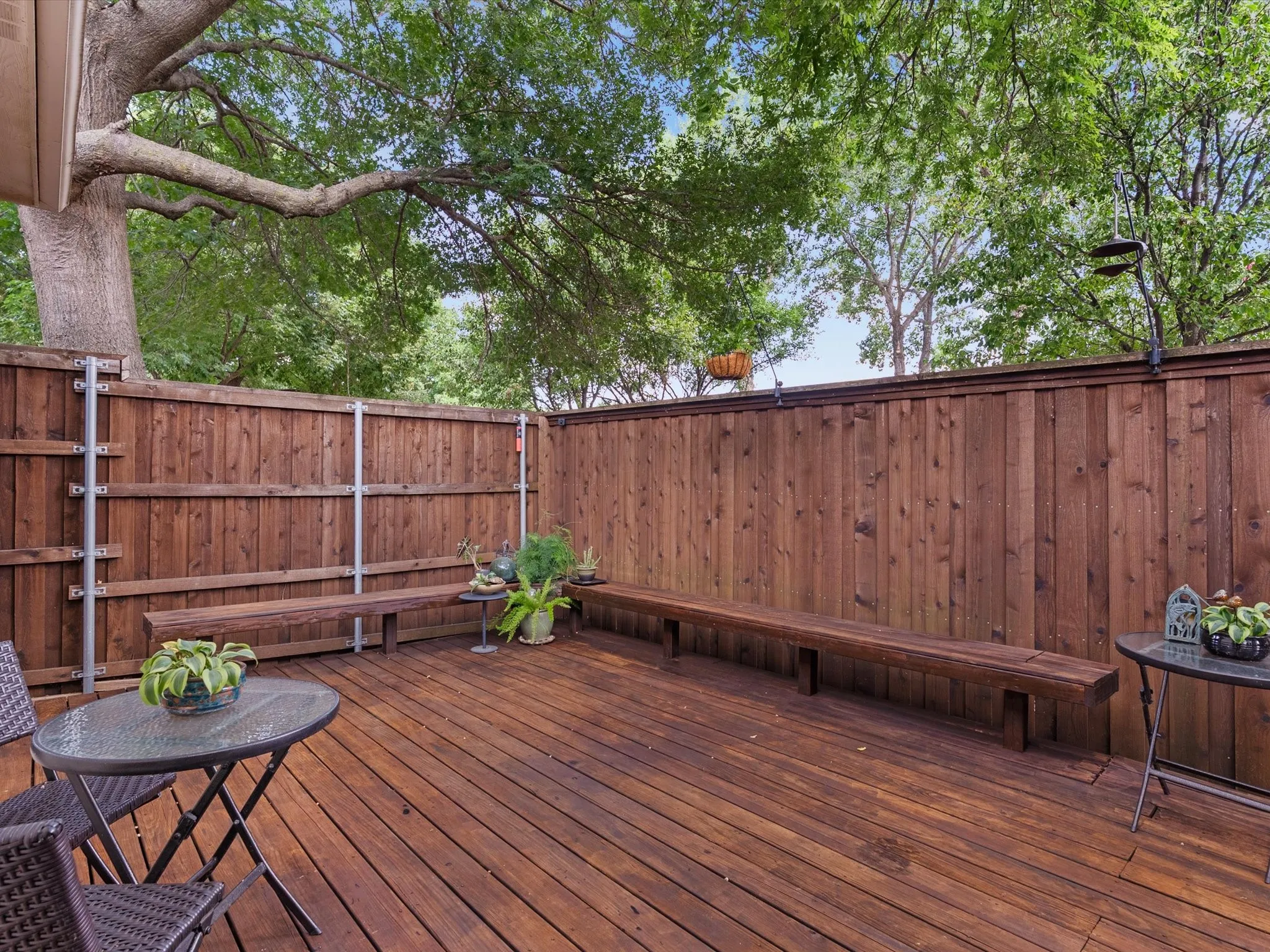 Spacious wooden deck featuring integrated bench seating, privacy fencing, and mature trees providing natural shading