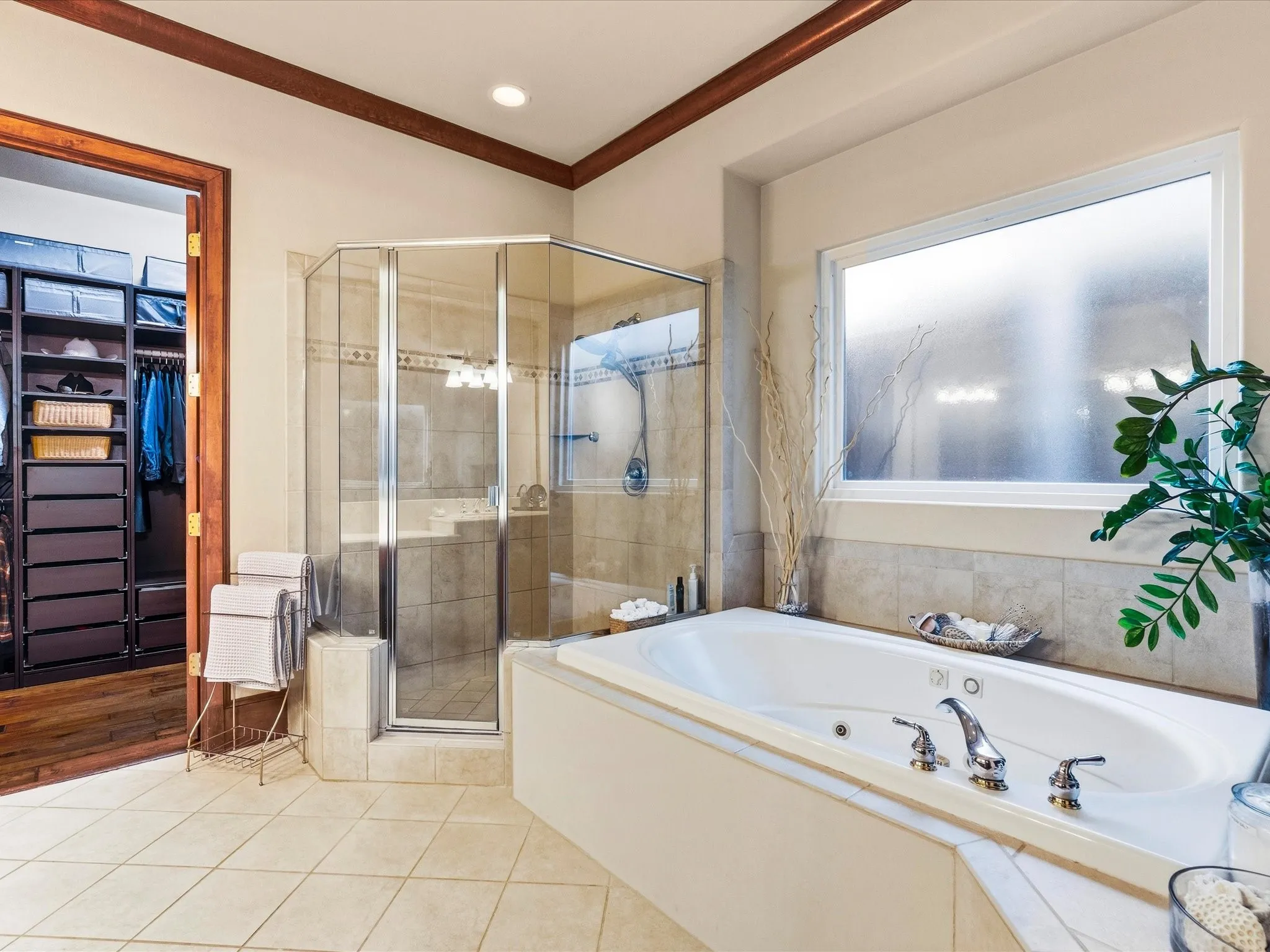Spacious bathroom featuring a built-in jetted tub, a glass-enclosed shower with tiled walls, and light-toned tile flooring