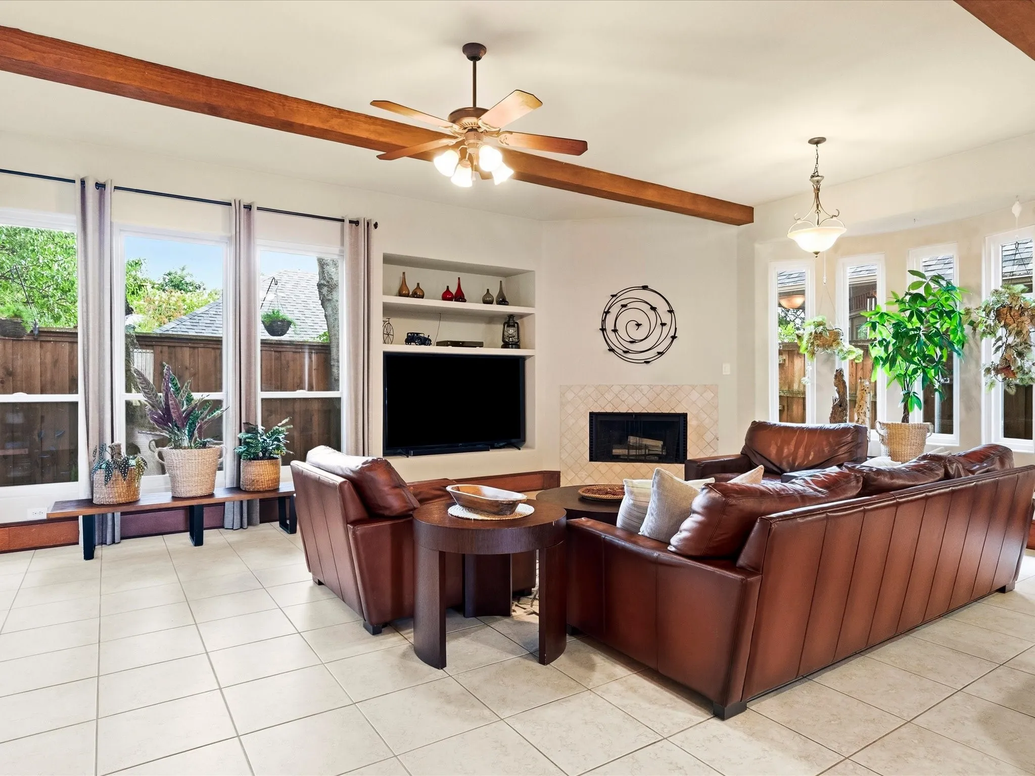 Spacious living area featuring light-toned square tile flooring, exposed wood ceiling beams, and a fireplace with a tiled surround