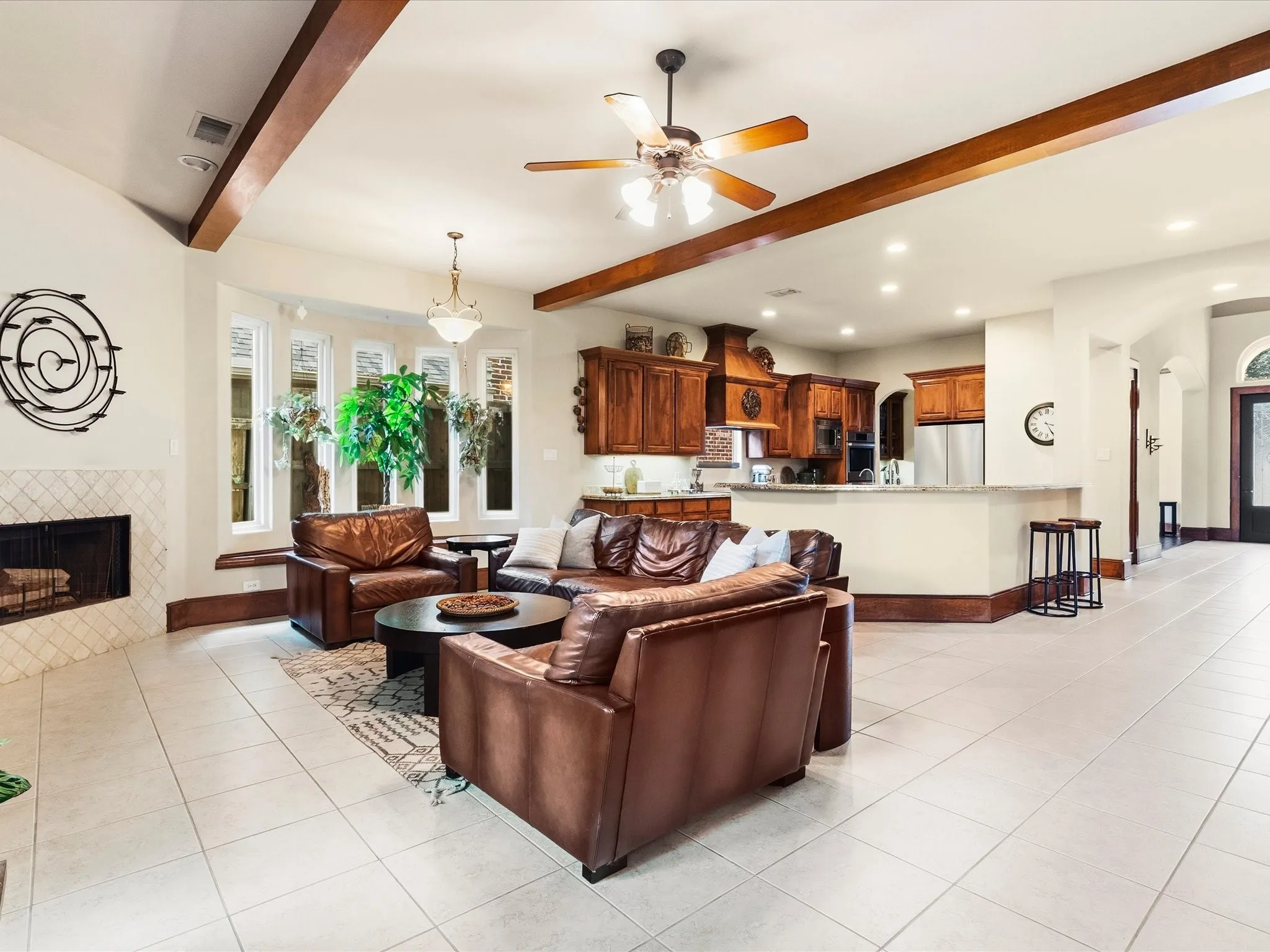 Spacious interior with neutral tile flooring, a fireplace featuring a diamond-patterned tile surround, and a kitchen with warm wood cabinetry