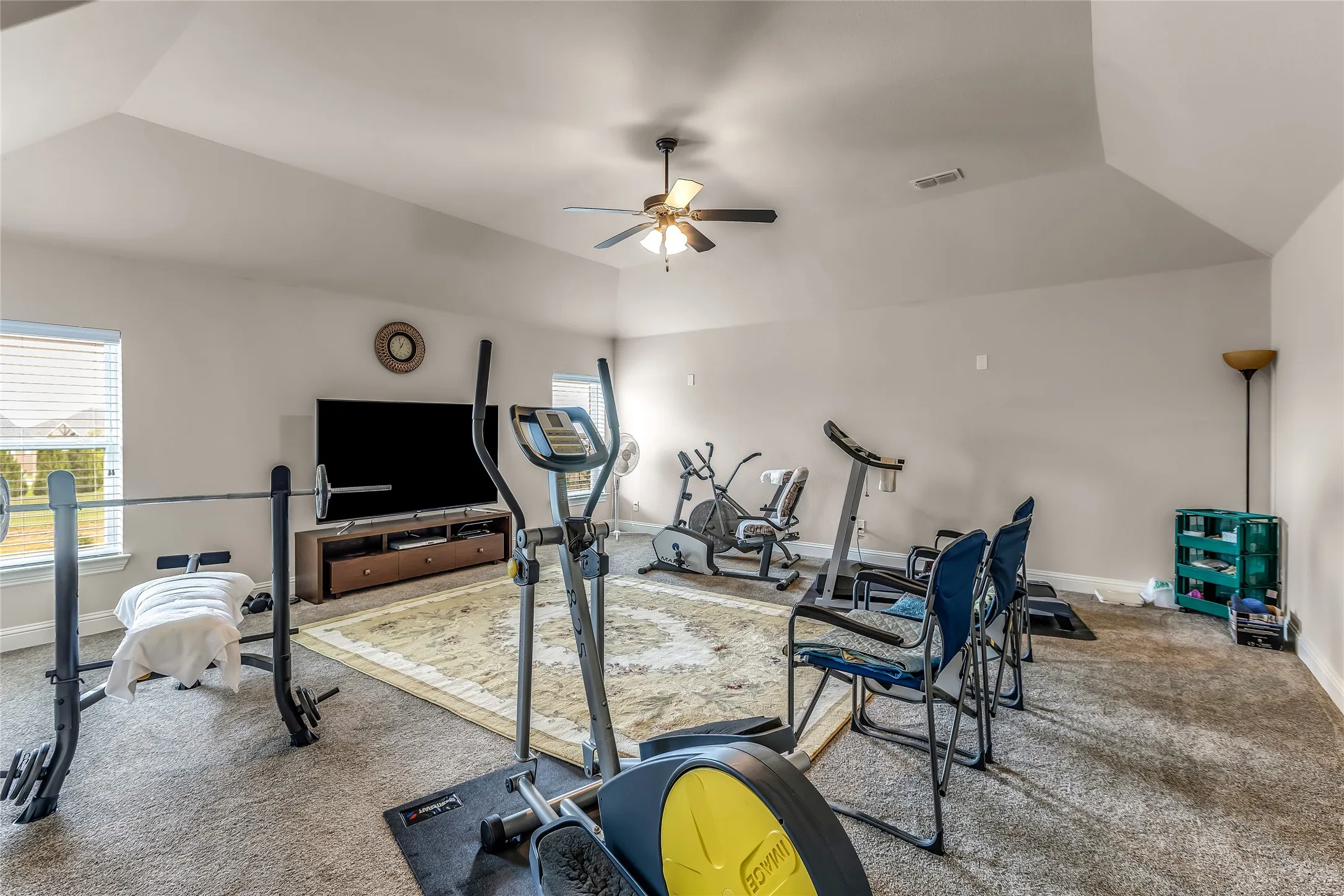 Expansive bonus room featuring vaulted ceilings, ceiling fan, carpeted flooring, and multiple windows with blinds