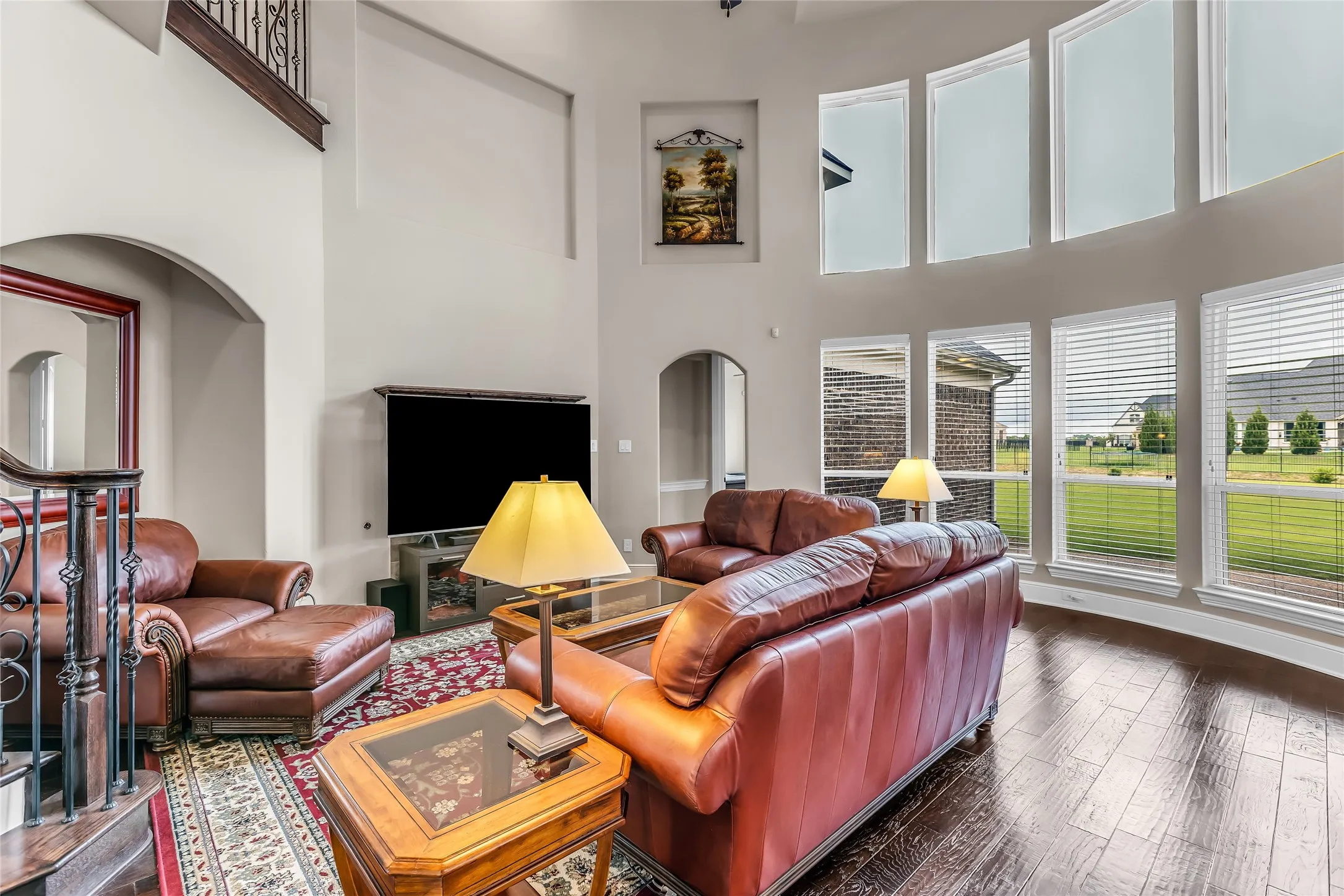 Two-story living area featuring wood-finish flooring, a grand staircase with wrought iron balusters, high ceilings, arched doorways, and a wall of windows
