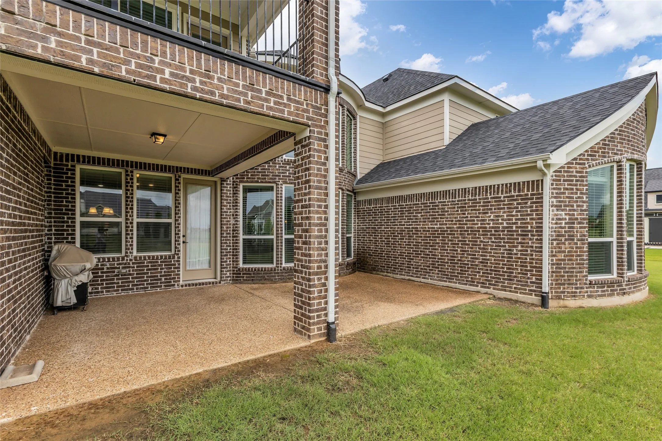 Covered outdoor patio with exposed aggregate concrete flooring, brick exterior, and a second-story balcony overhead
