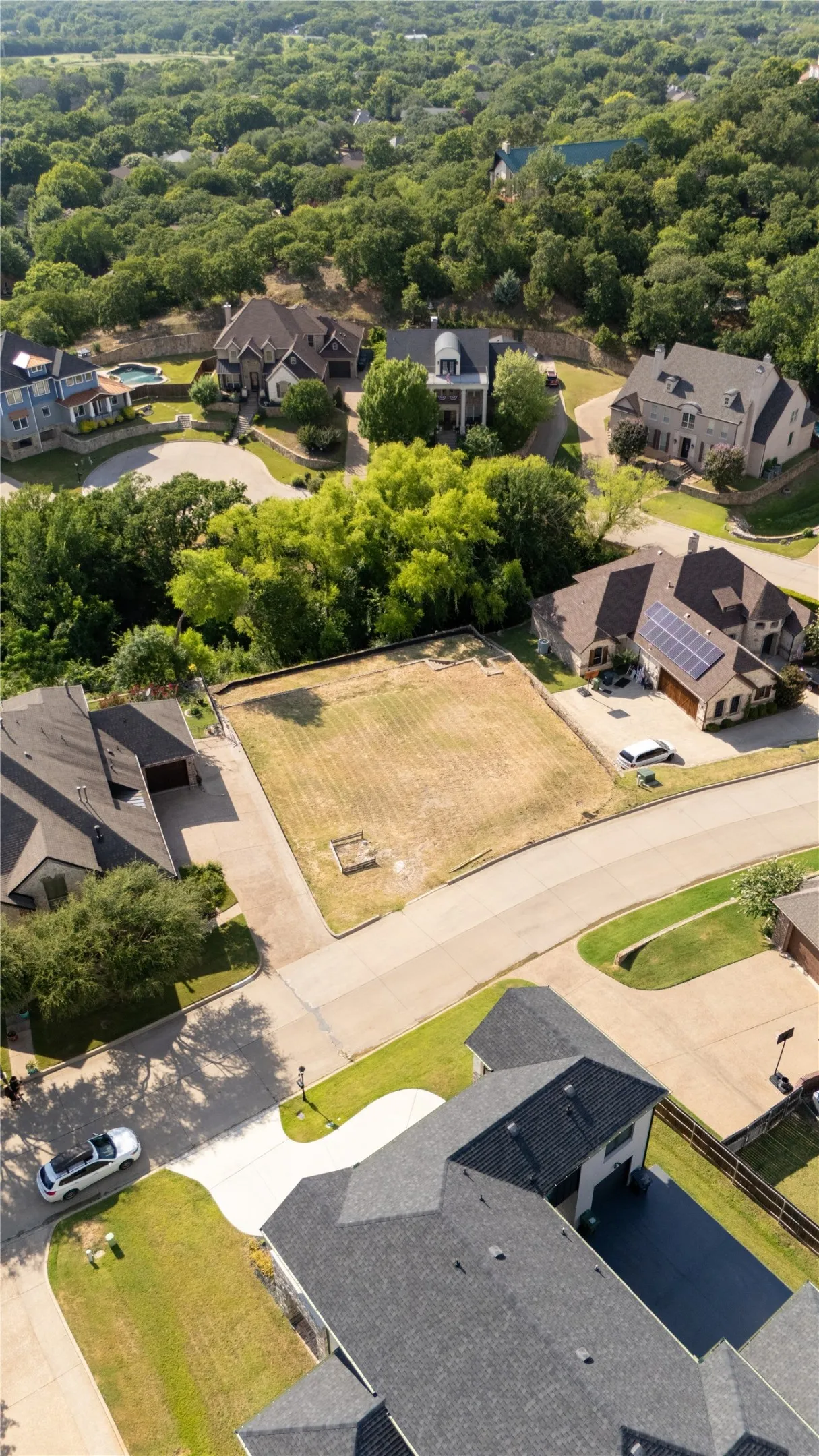 Cleared lot featuring a grass surface, surrounded by mature trees and residential properties