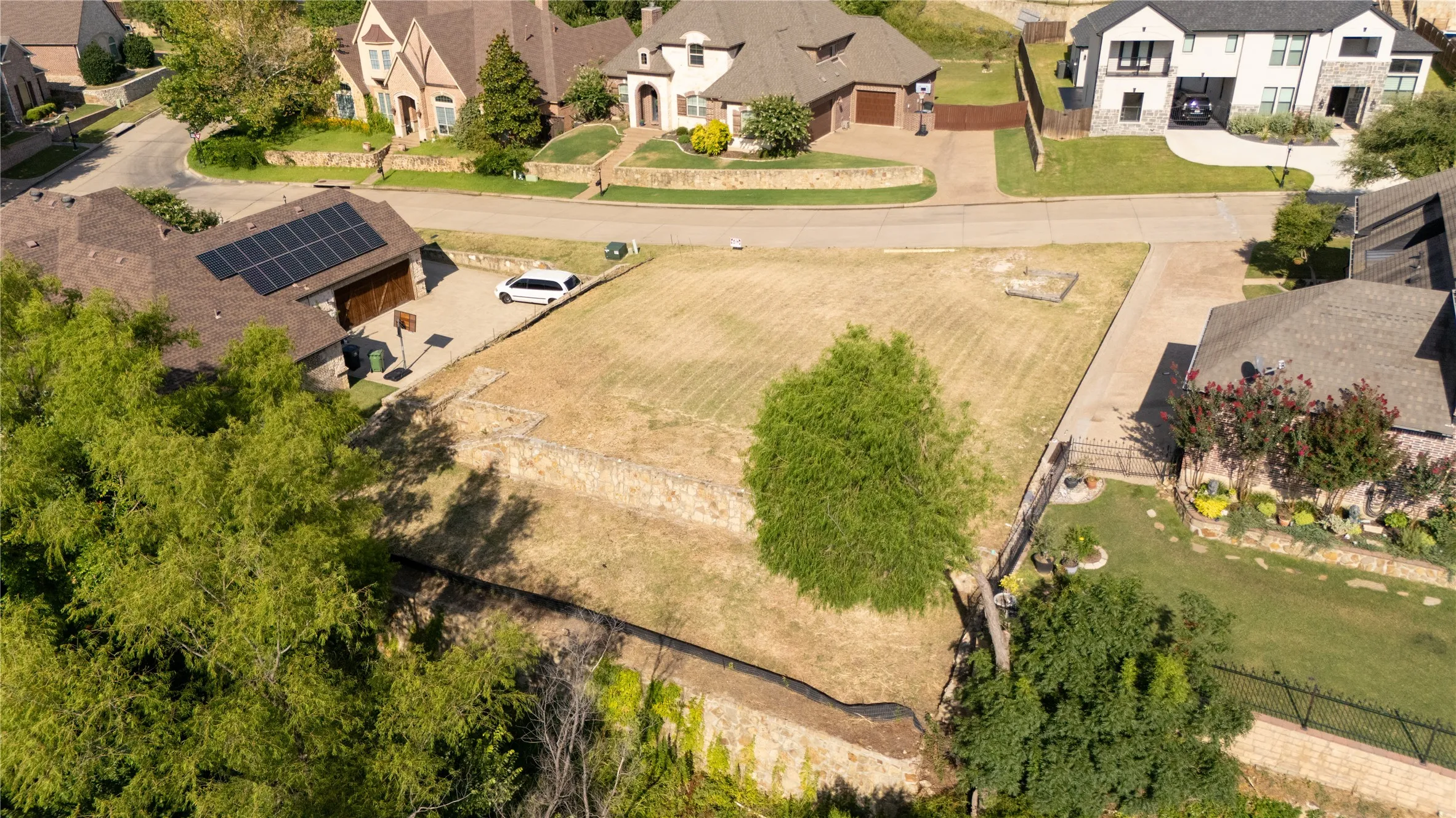 Expansive vacant lot featuring a gentle slope, mature trees, and established neighborhood setting