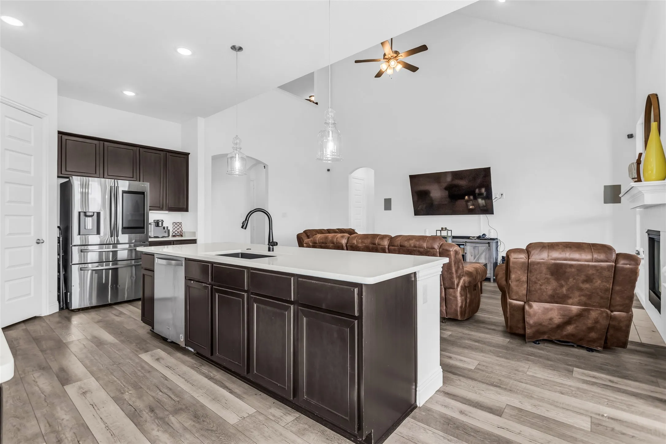 Kitchen featuring dark brown cabinetry, arched walkways, appliances with stainless steel finishes, open floor plan, and pendant lighting
