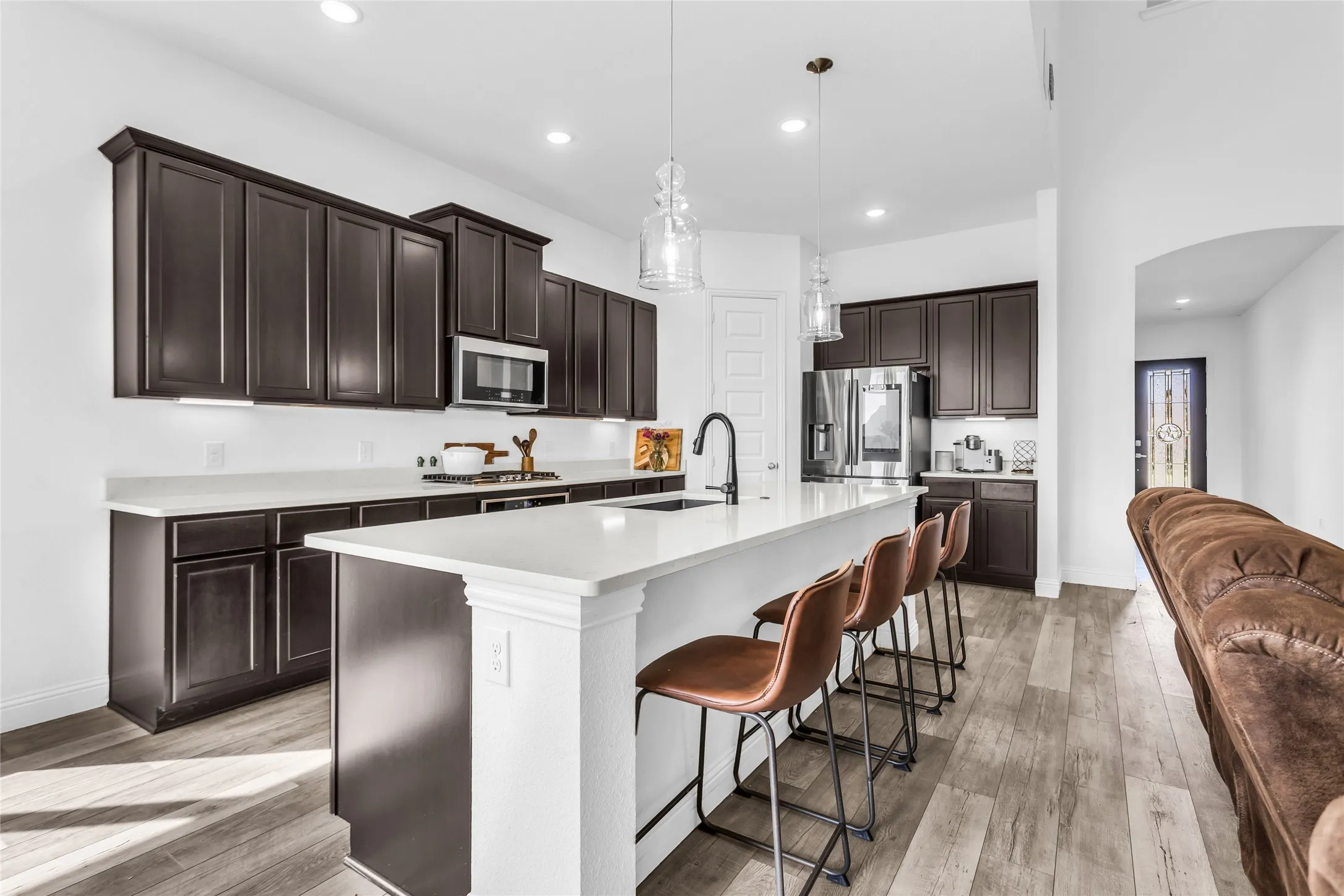 Kitchen featuring dark brown cabinetry, arched walkways, hanging light fixtures, a breakfast bar, and recessed lighting