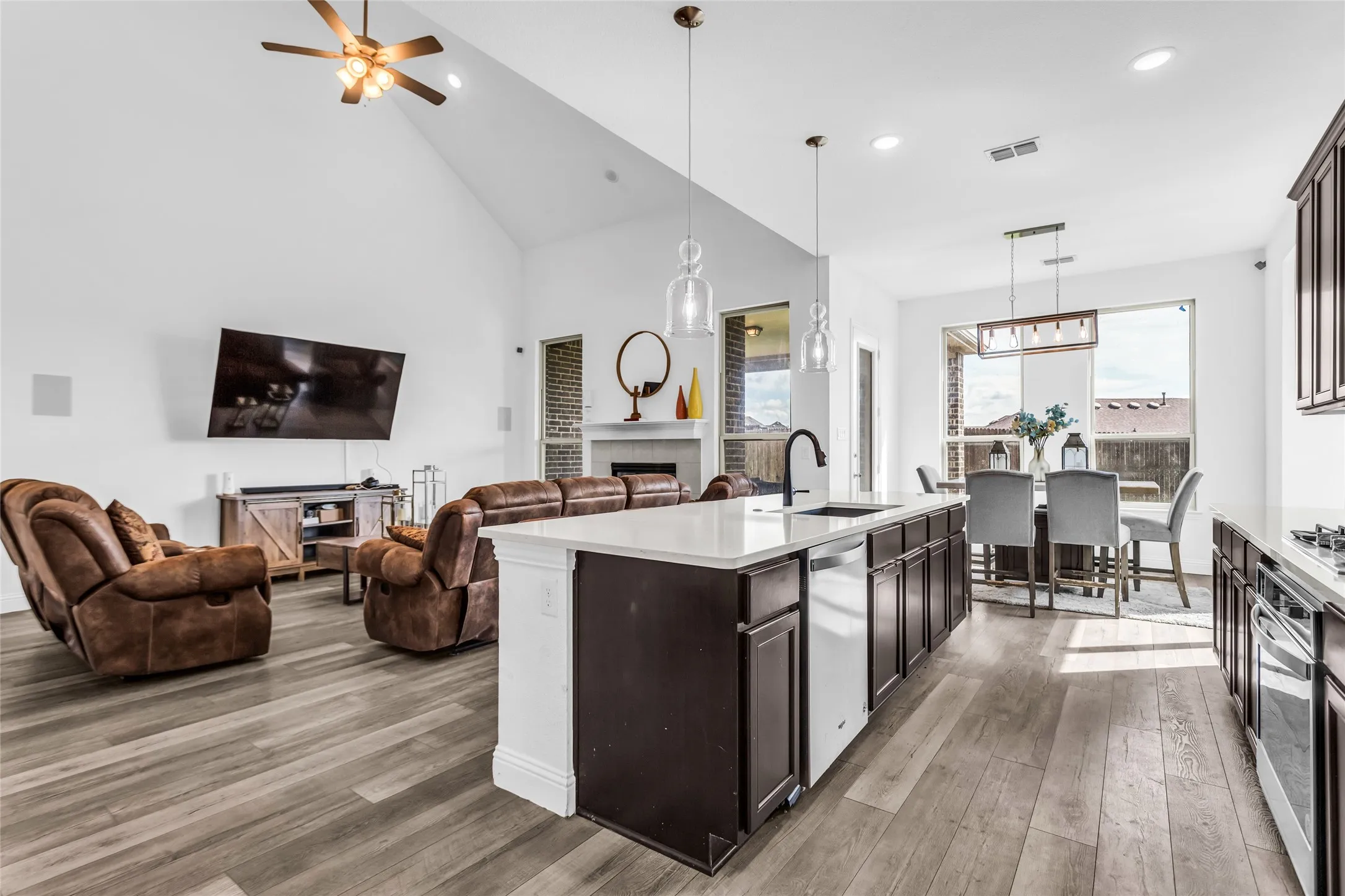 Kitchen with open floor plan, dark brown cabinetry, light wood-style floors, hanging light fixtures, and an island with sink