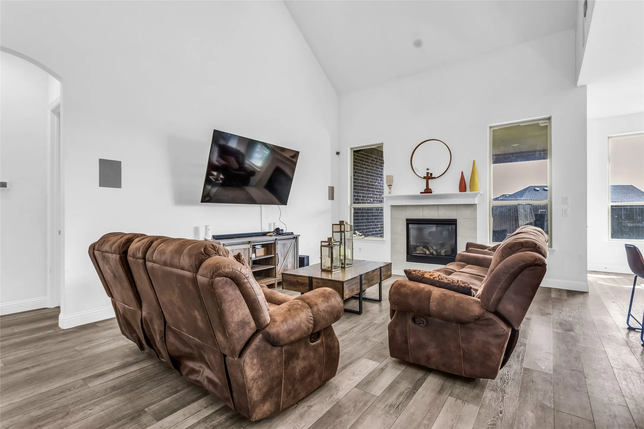 Living area with high vaulted ceiling, a tile fireplace, wood finished floors, and arched walkways