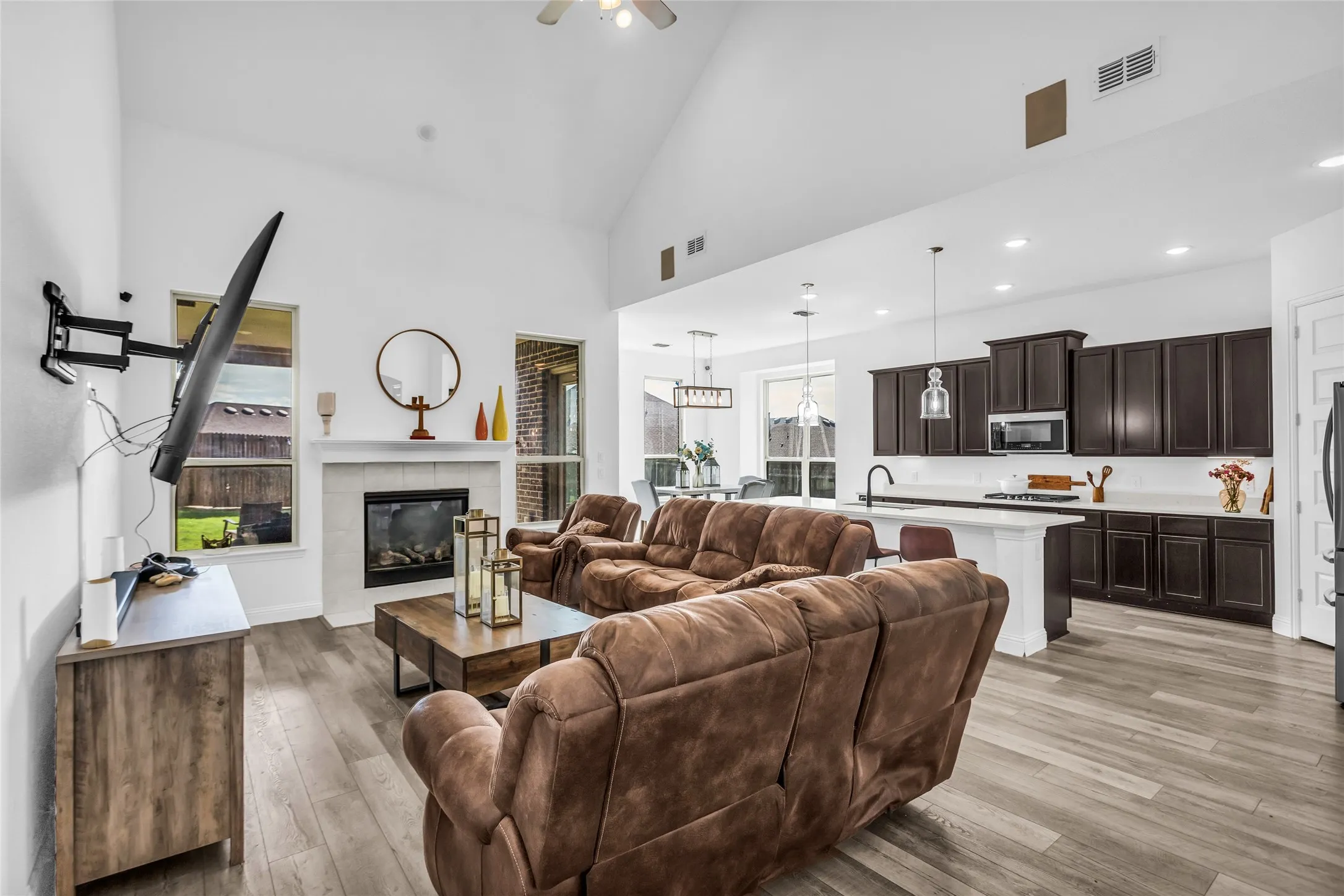 Living room with high vaulted ceiling, light wood-style floors, a tiled fireplace, a ceiling fan, and recessed lighting