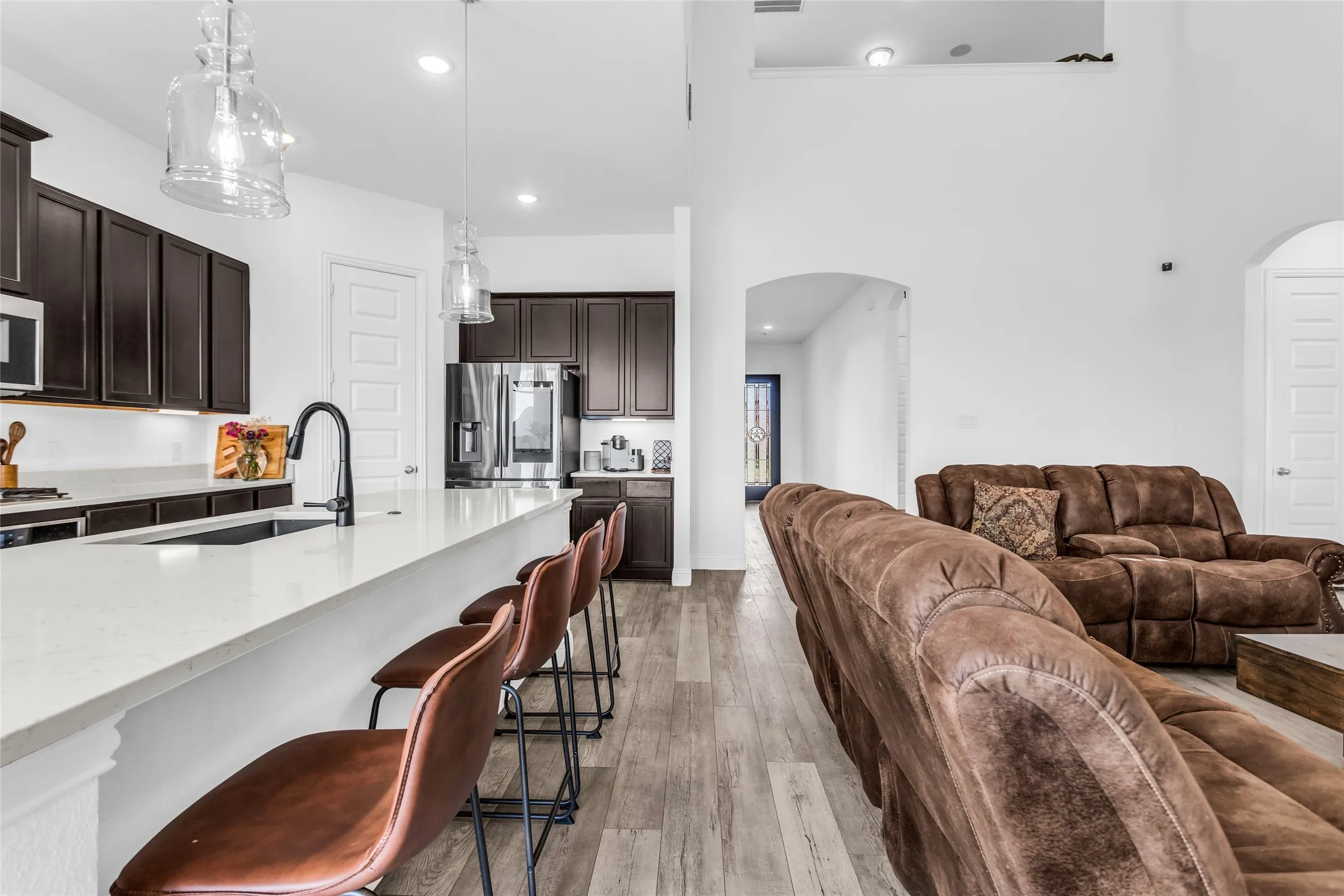 Kitchen featuring dark brown cabinets, light wood-type flooring, hanging light fixtures, light stone counters, and recessed lighting