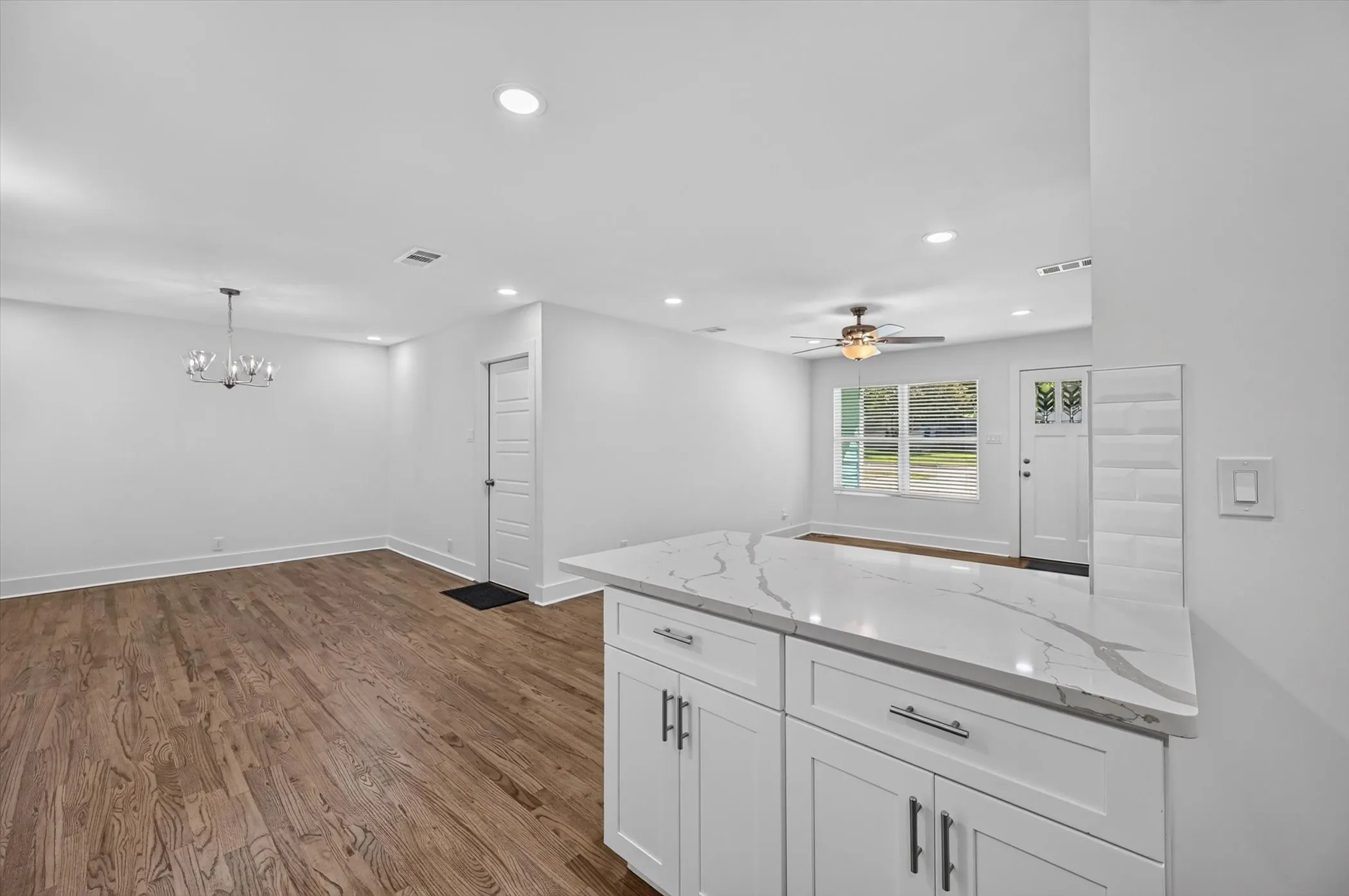 Open-concept living area featuring wood-finish flooring, recessed lighting, and a modern chandelier