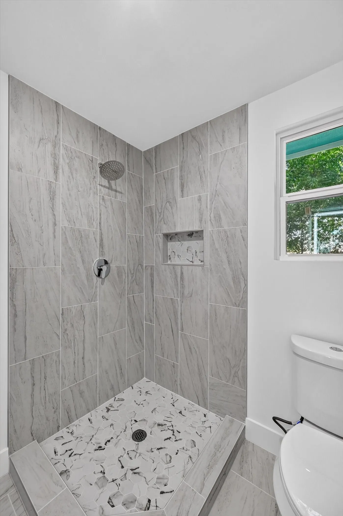 Corner shower stall featuring large format grey tile walls with a built-in niche
