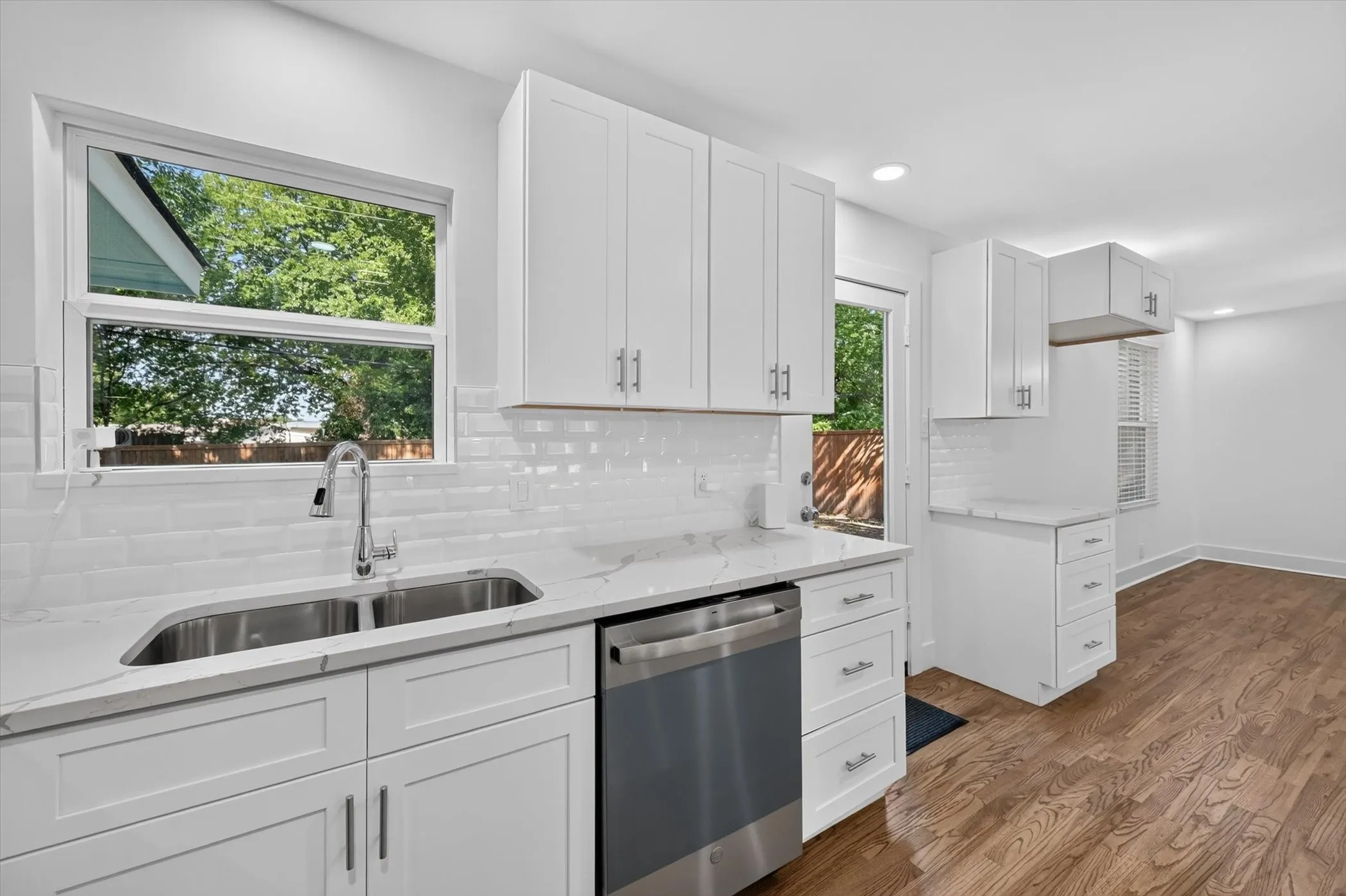 Kitchen featuring white shaker cabinetry, stainless steel double basin sink, stainless steel dishwasher, white subway tile backsplash, and wood-finish flooring