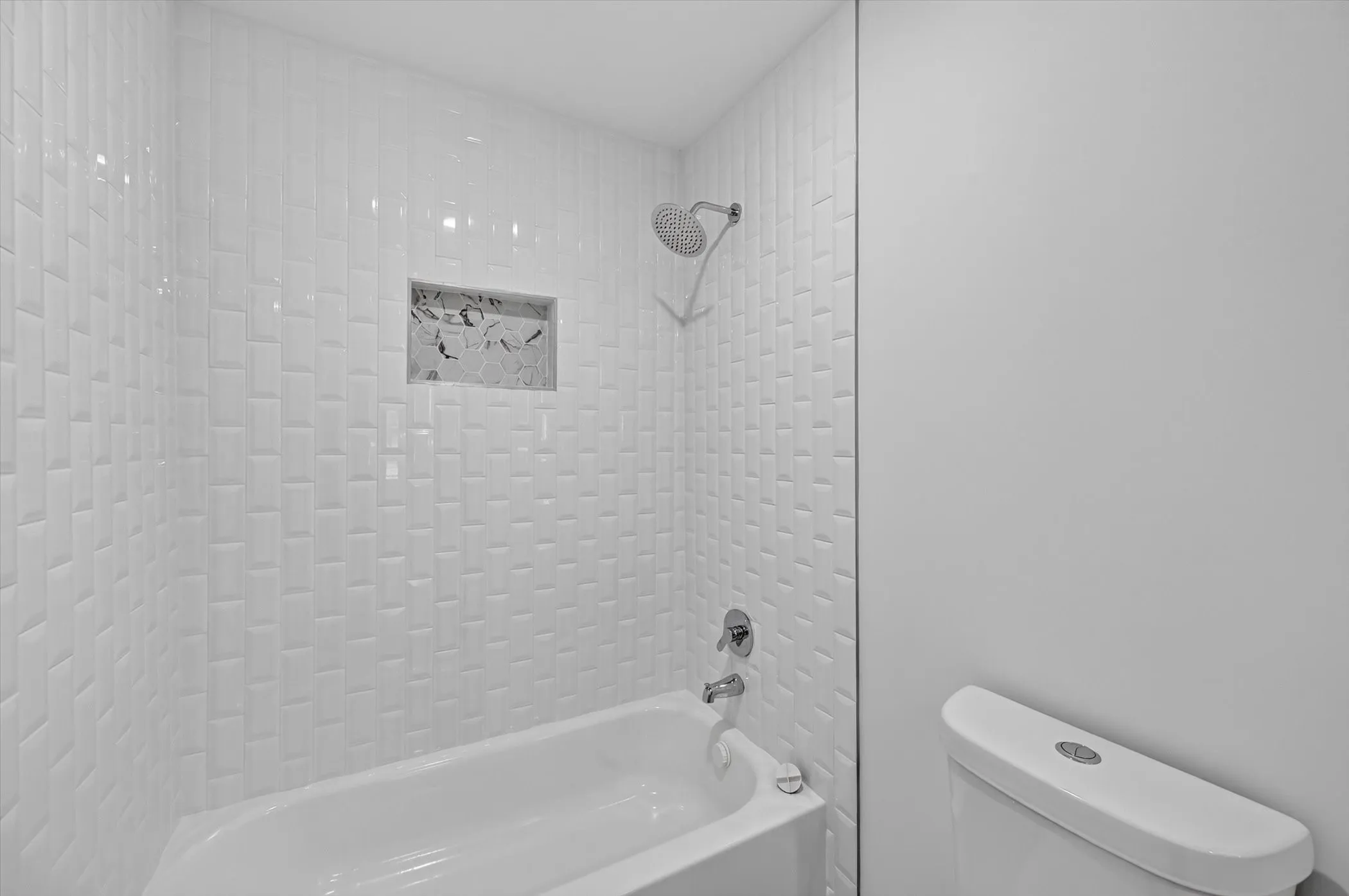 Bathtub and shower combination featuring white subway tile surround, a built-in shower niche with stone-finish tile, and a chrome shower head and faucet
