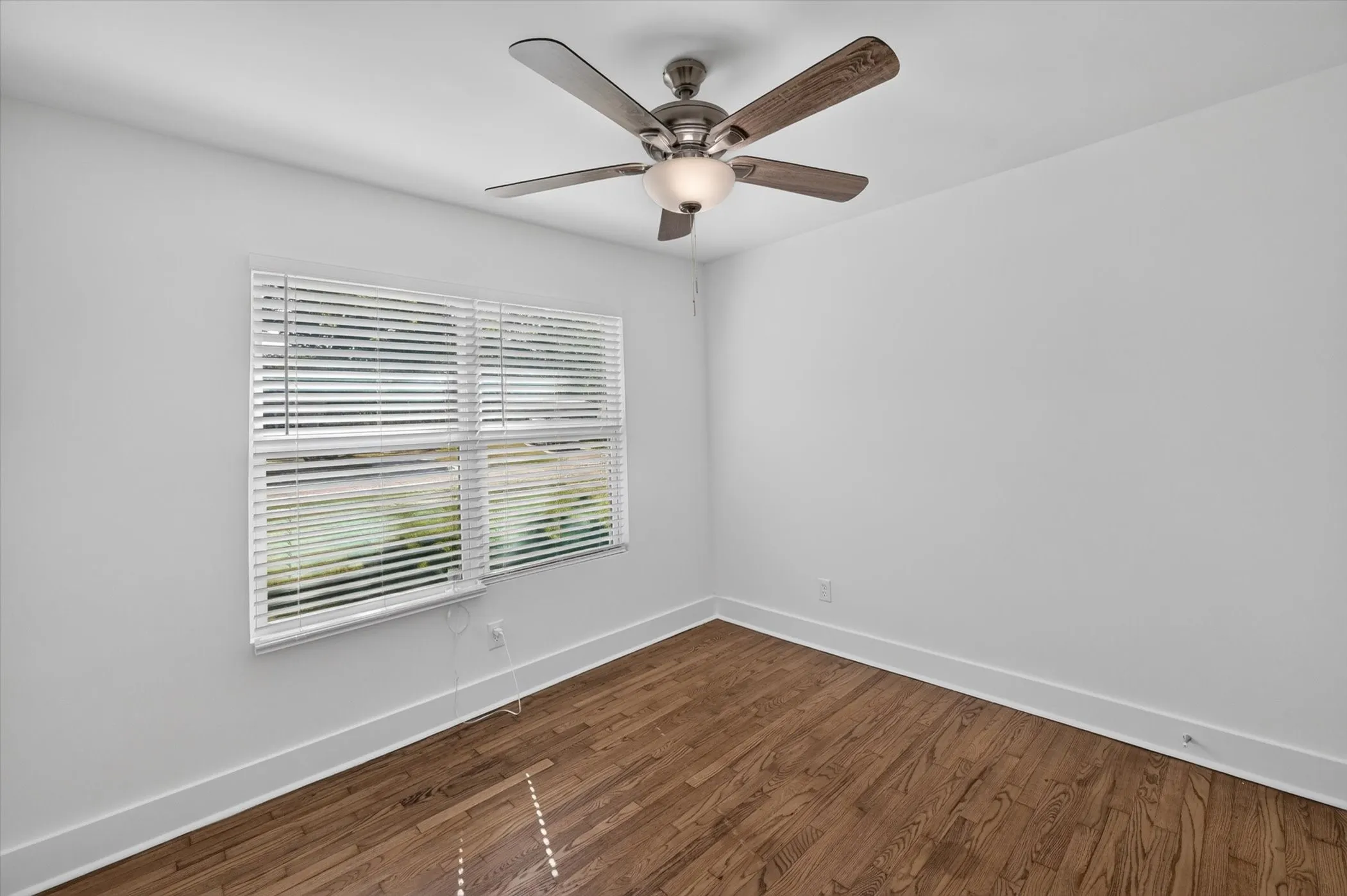 Bright interior space featuring wood-finish flooring, white baseboards, and a ceiling fan with integrated lighting