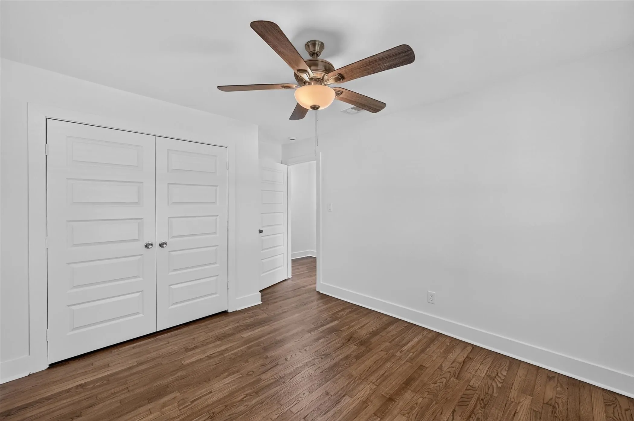 Wood-finish flooring throughout, bright white walls, a ceiling fan with light fixture, and panel doors with brushed nickel hardware