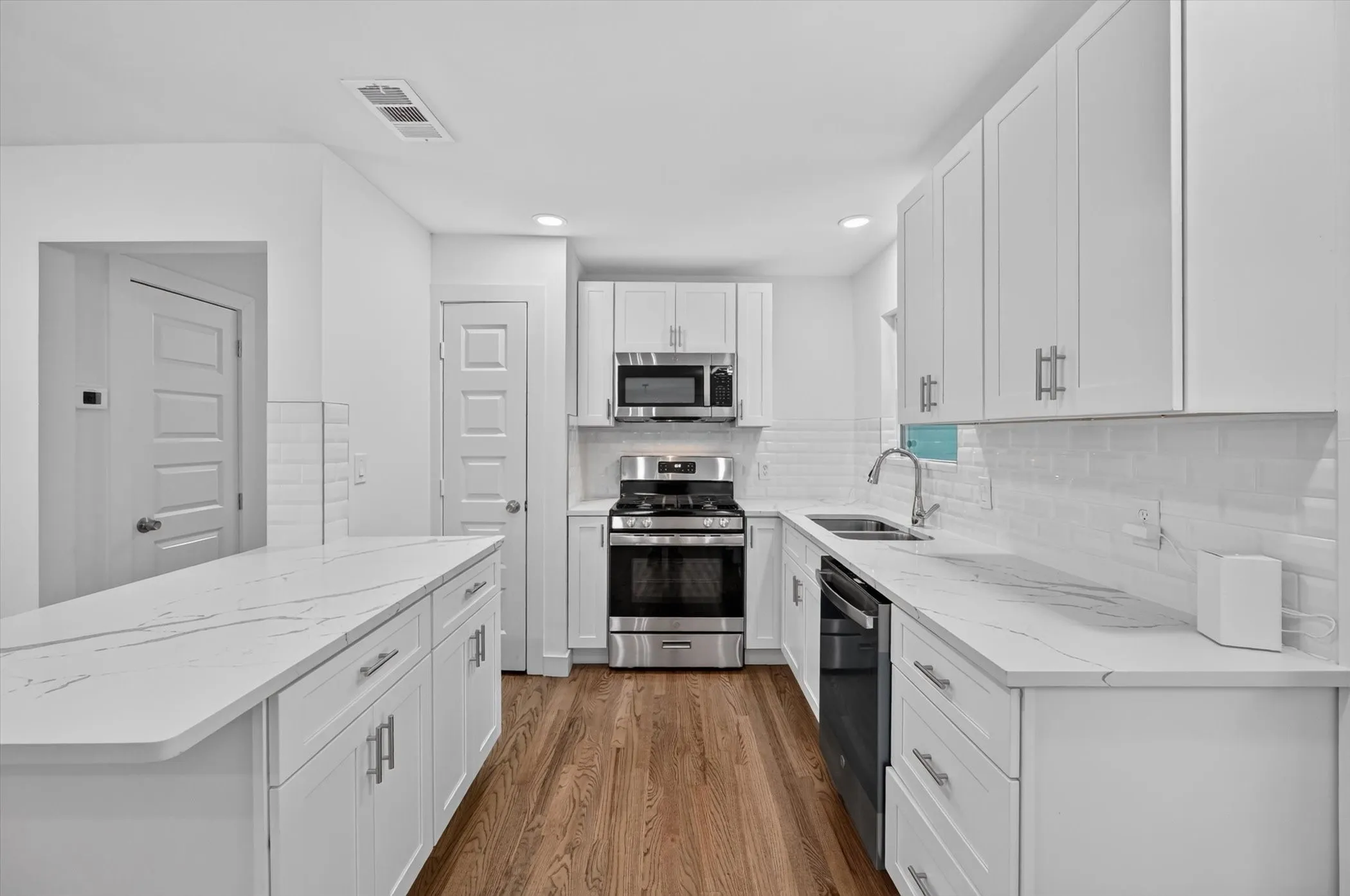 Kitchen featuring a central island with a stone-finish countertop, white shaker cabinetry, stainless steel appliances, a subway tile backsplash, and wood-finish flooring