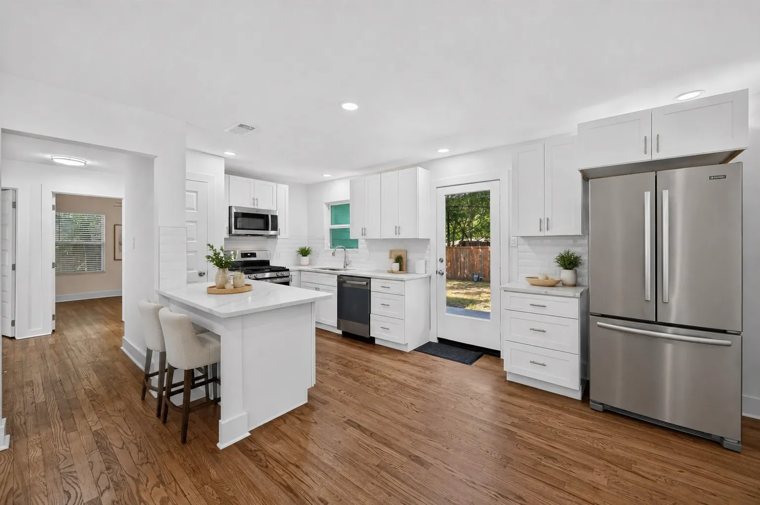 Virtually staged..Bright kitchen featuring white shaker cabinetry, stainless steel appliances, a white subway tile backsplash, a large kitchen island with counter seating, and wood-finish flooring