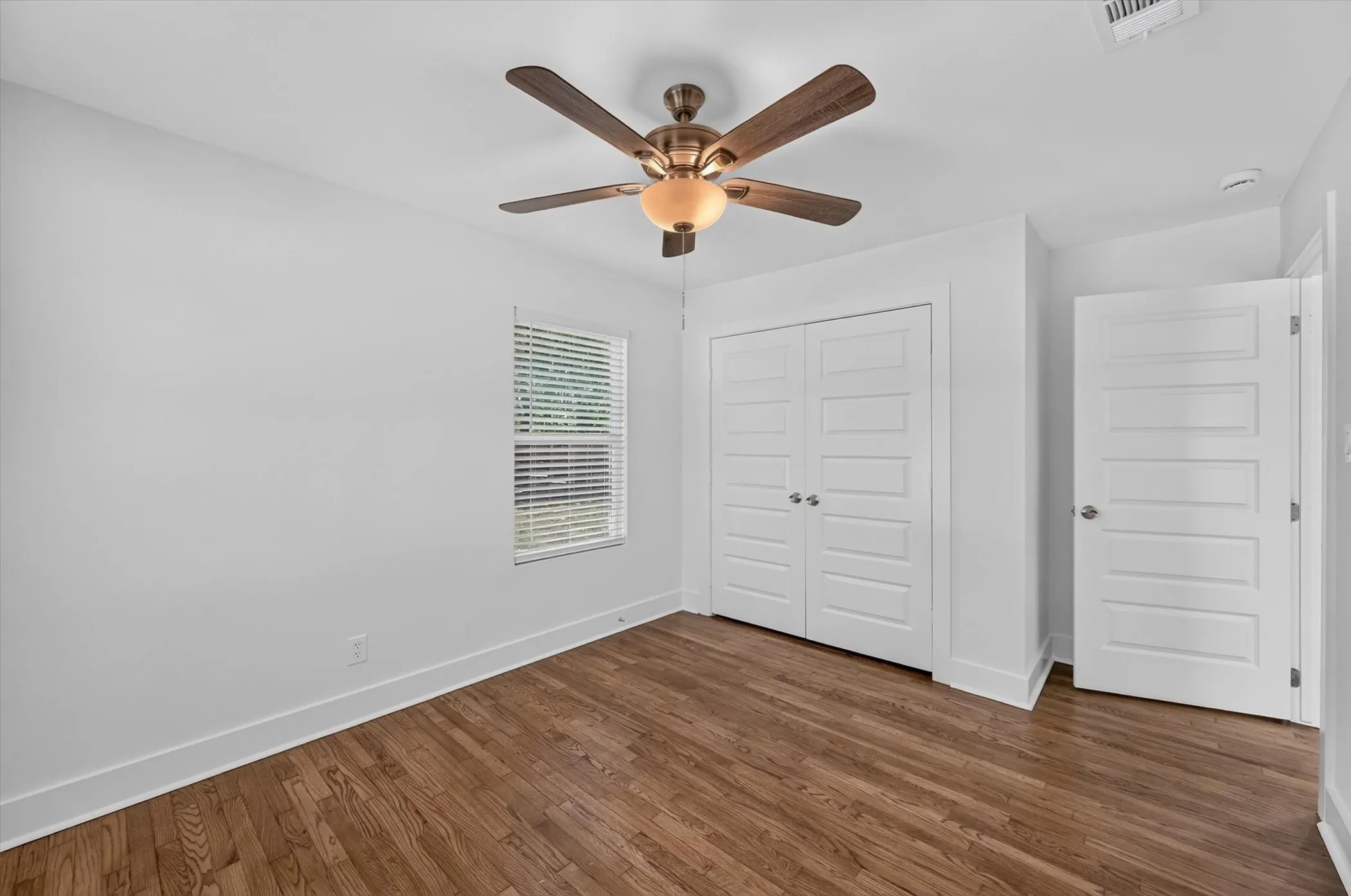 Interior room featuring wood-finish flooring, white walls, and a ceiling fan with integrated lighting