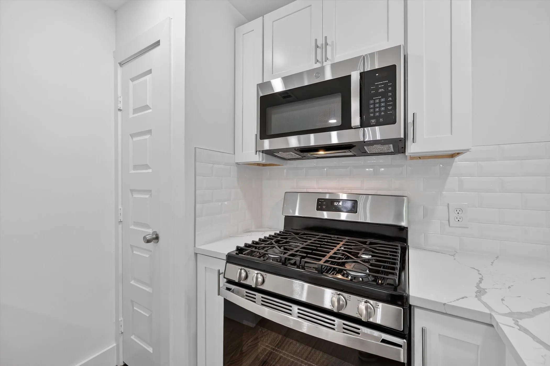 Kitchen featuring stainless steel range, built-in microwave, white shaker cabinetry, white subway tile backsplash, and light-colored countertops with veining