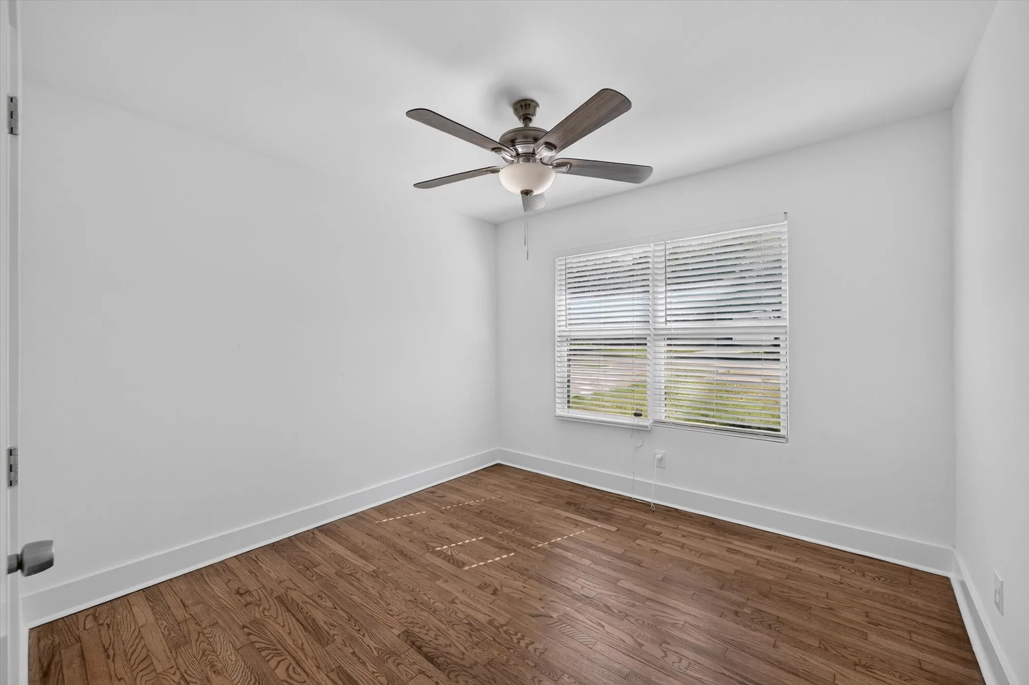 Room with wood-finish flooring, a ceiling fan with integrated lighting, and a window featuring horizontal blinds