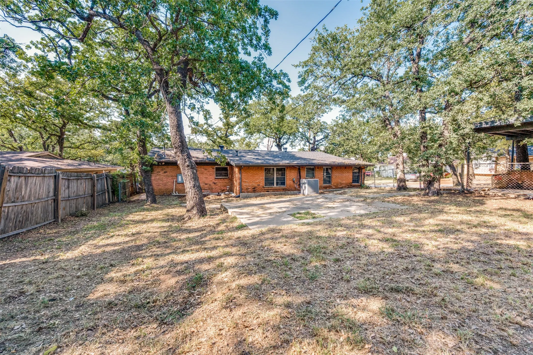 Spacious backyard with mature trees, a concrete patio, and a brick exterior