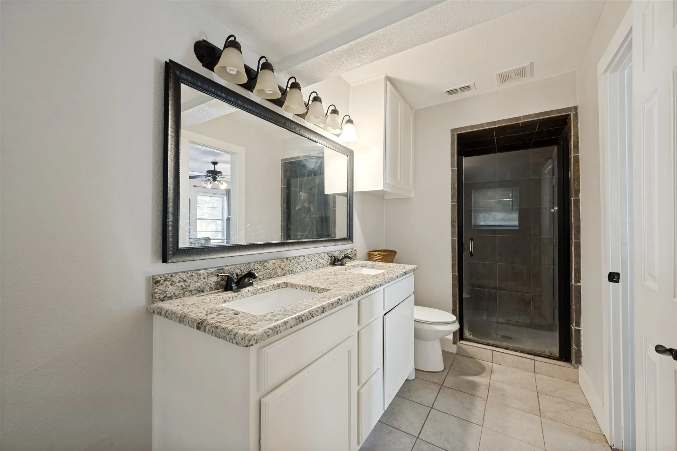 Bathroom featuring a dual-sink vanity with a light-toned countertop, a large framed mirror, and a walk-in shower with a glass door