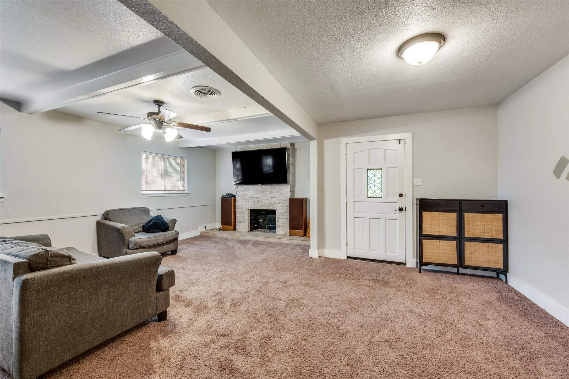 Spacious living area featuring neutral-toned walls, textured carpeting, and a ceiling fan with integrated lighting