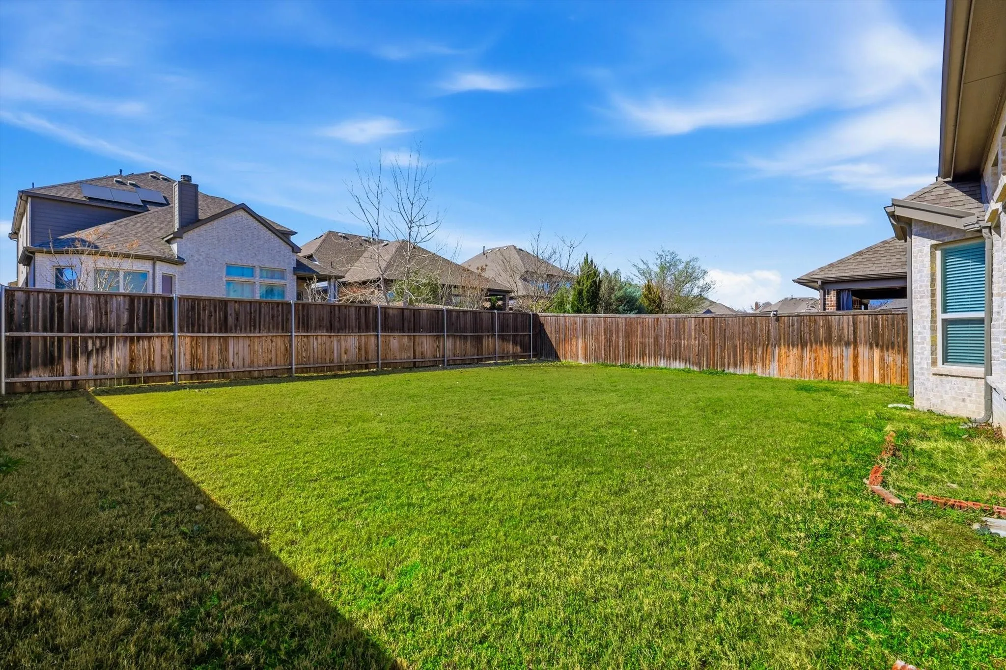 Spacious backyard featuring a manicured lawn, full wood privacy fencing, and a light-colored brick exterior