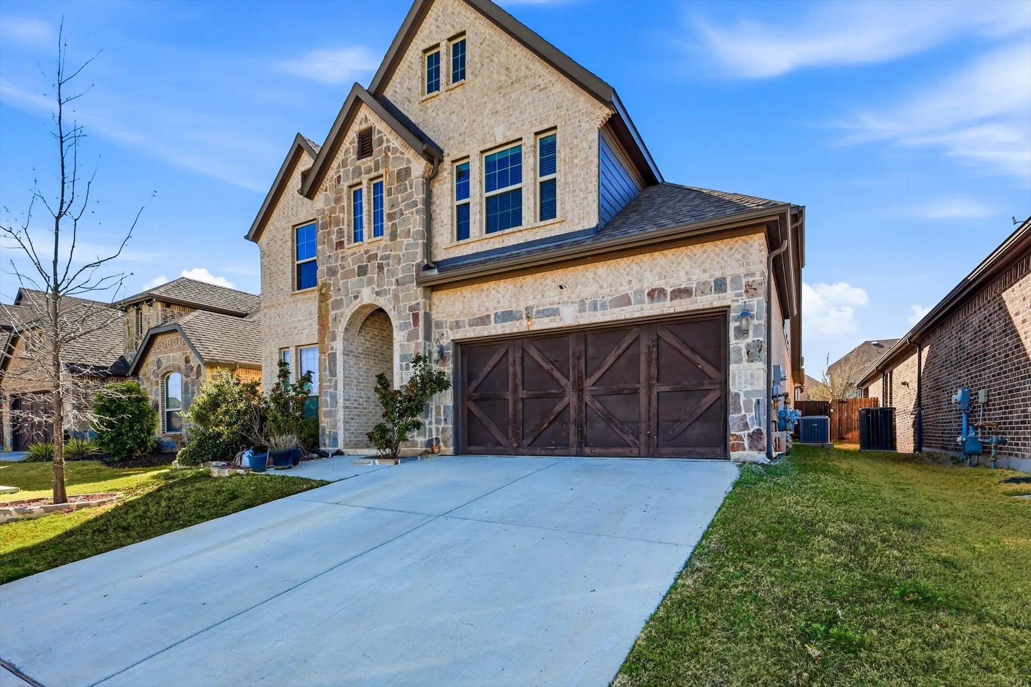 Exterior featuring a brick and stone facade, arched entry, multiple gabled rooflines, and a two-car garage with decorative wooden doors