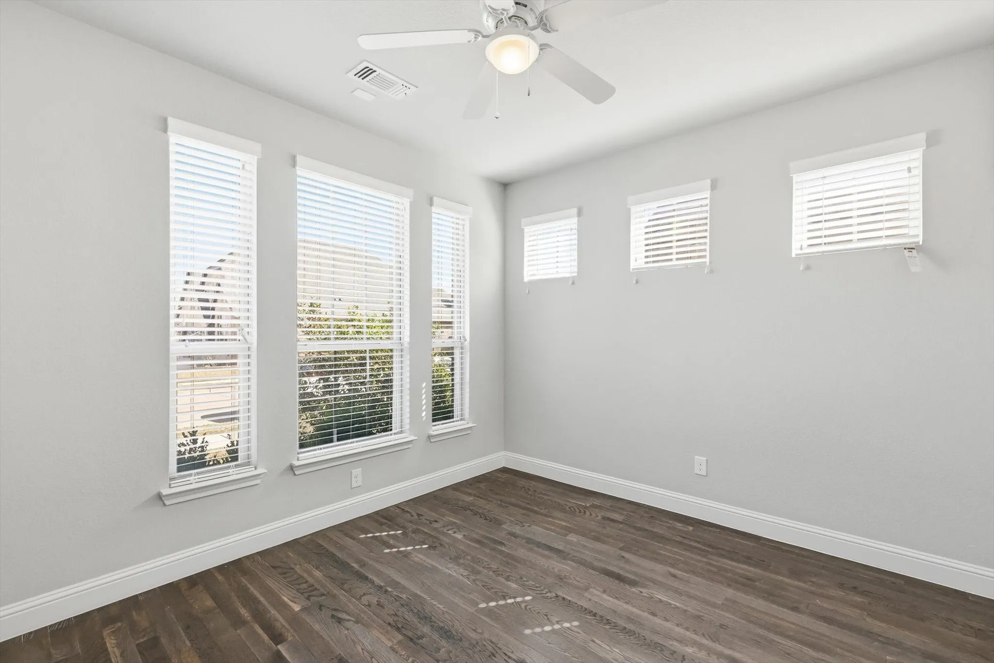 Room with wood-finish flooring, white walls, and multiple windows with blinds