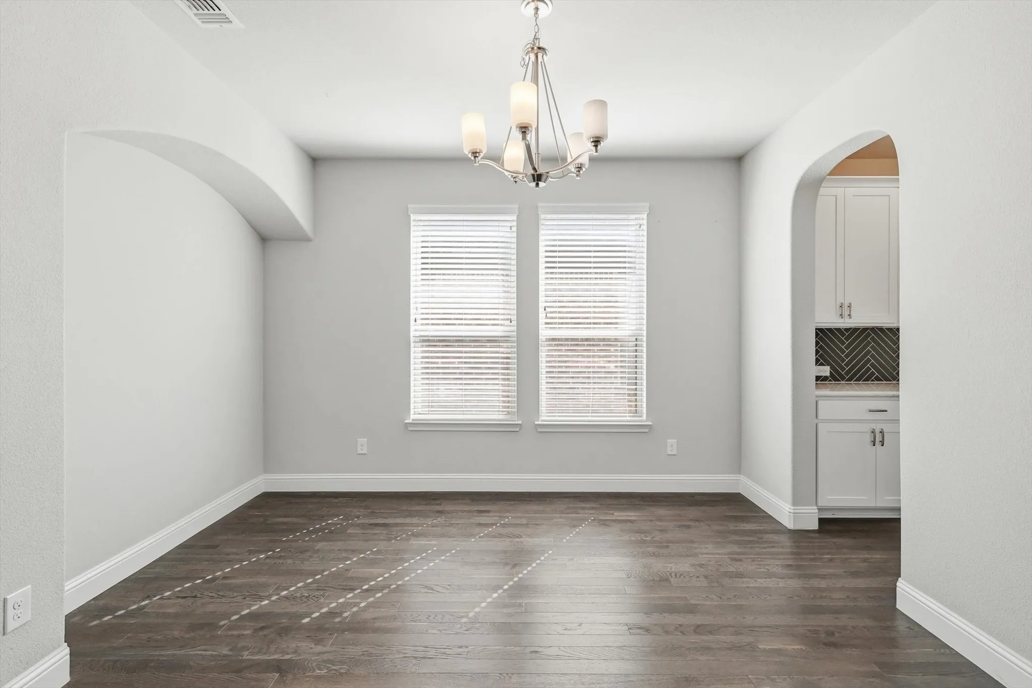 Spacious room featuring wood-finish flooring, bright overhead lighting, and two prominent windows