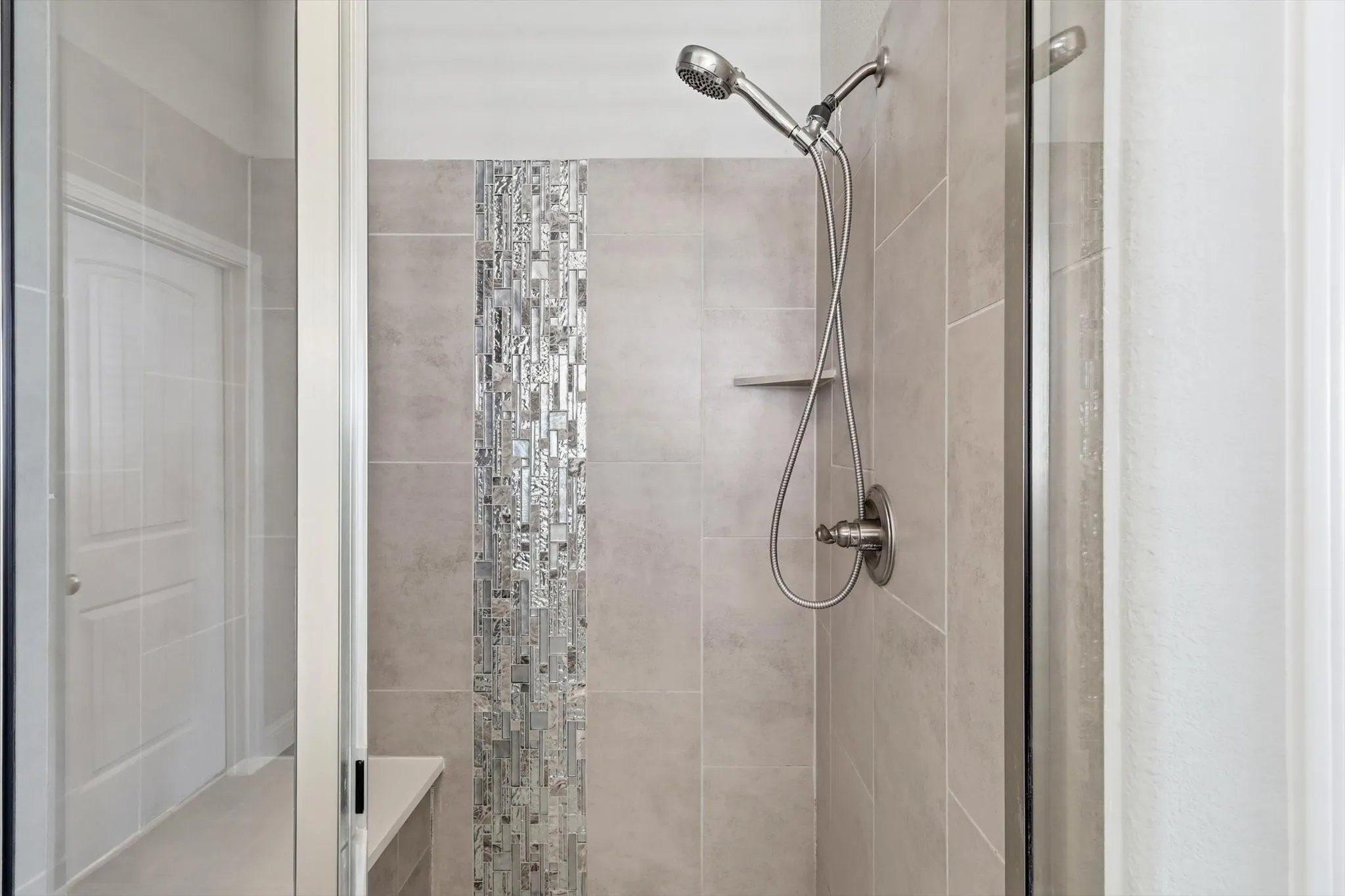 Walk-in shower with full-height tile surround, mosaic accent strip, built-in shelf, and brushed nickel fixtures