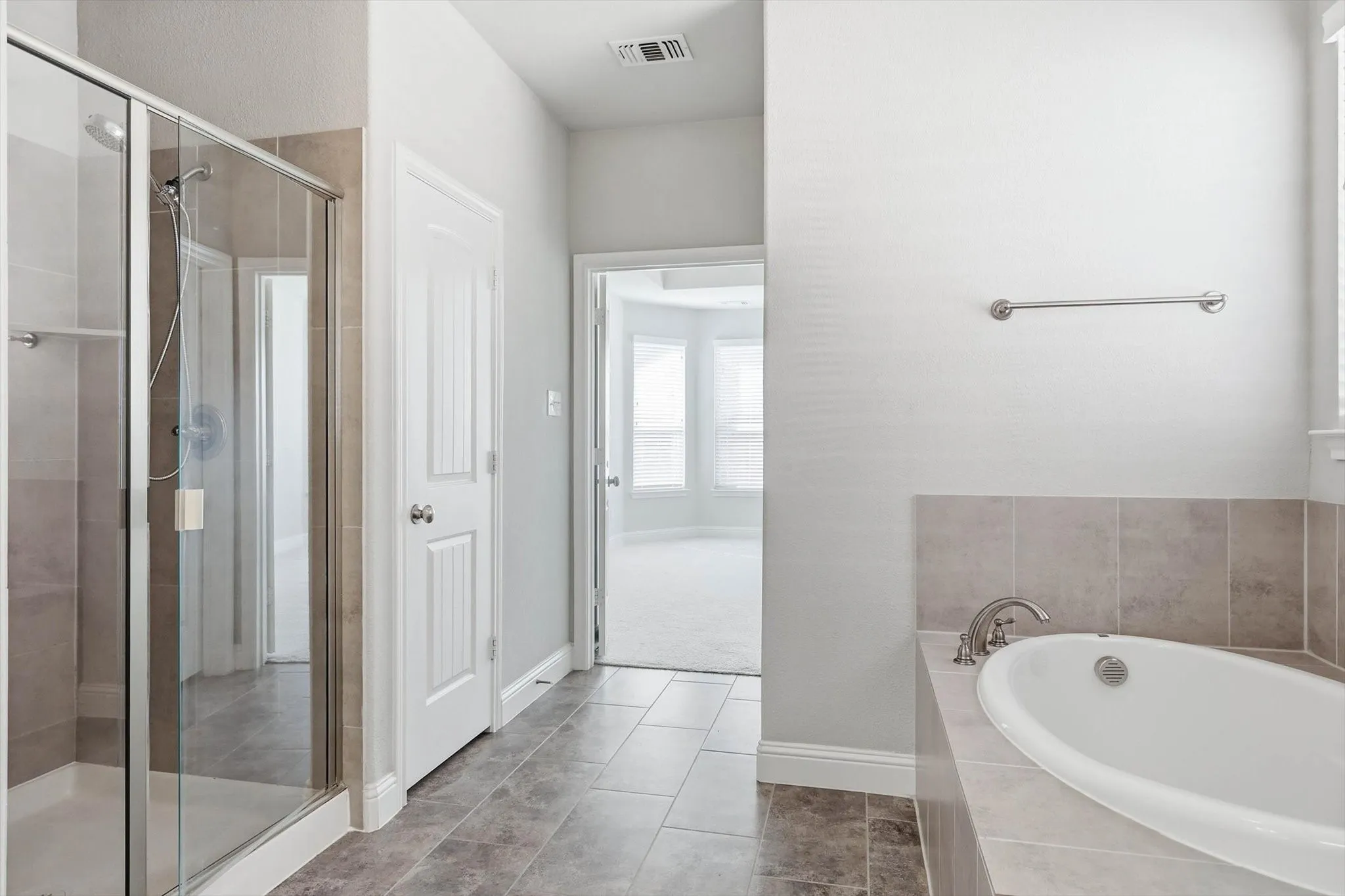 Spacious bathroom featuring a glass-enclosed shower, a separate soaking tub with tiled surround, and neutral floor tiling