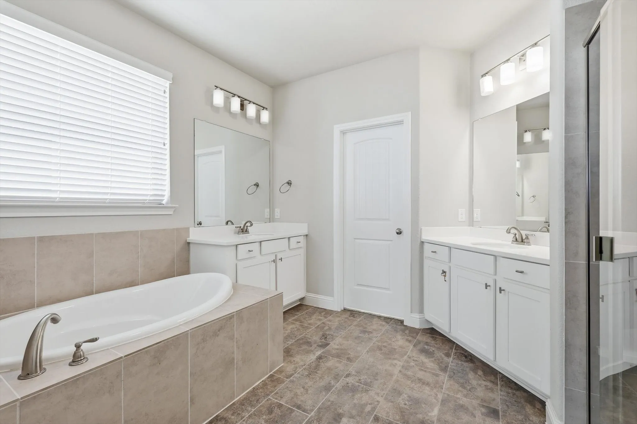 Bathroom featuring a built-in soaking tub, dual vanity sinks, white shaker-style cabinetry, and a glass-enclosed shower with tile surround