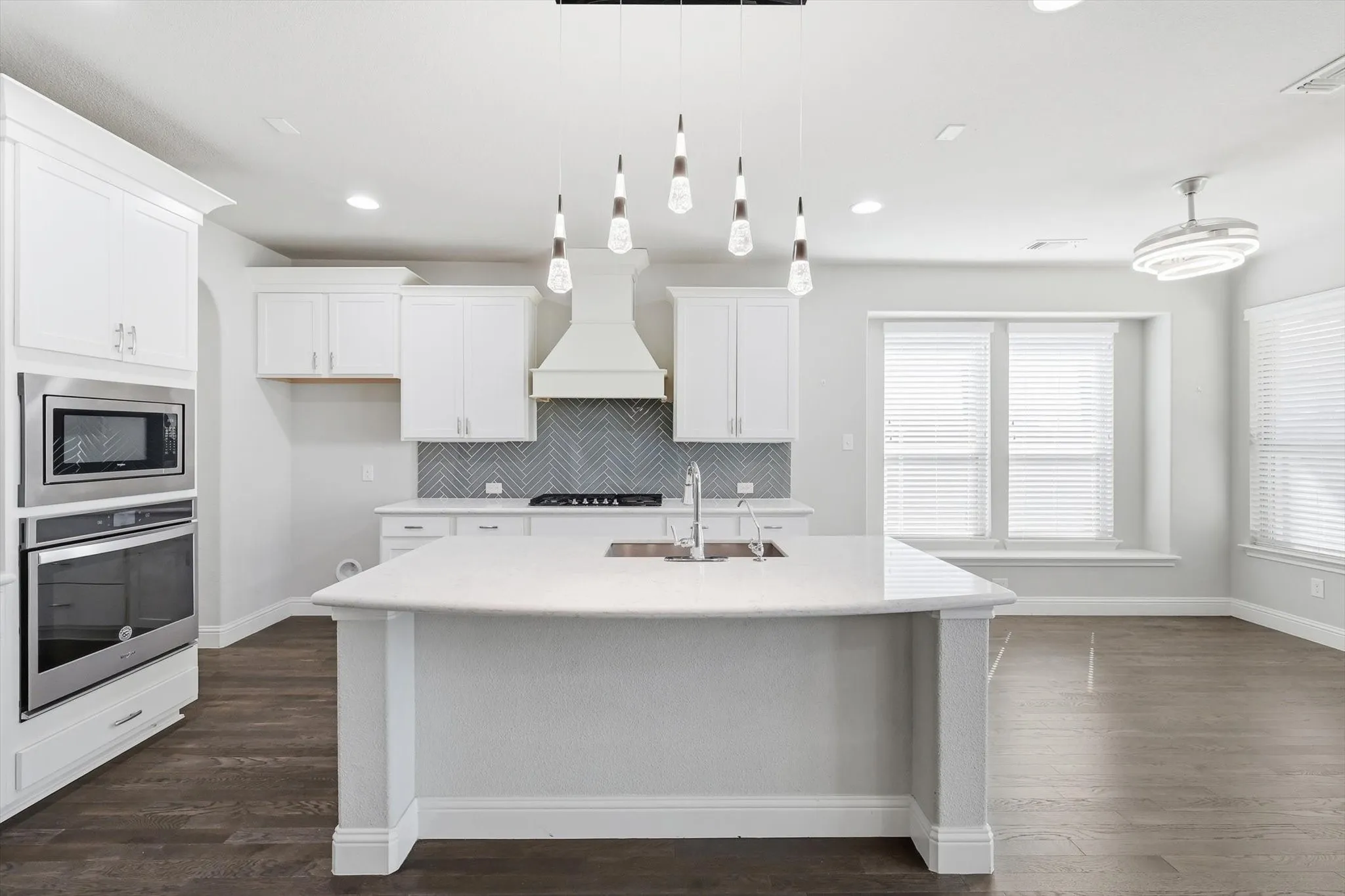 Kitchen featuring an expansive island with an undermount sink, white cabinetry, integrated stainless steel appliances, herringbone tile backsplash, and wood-finish flooring