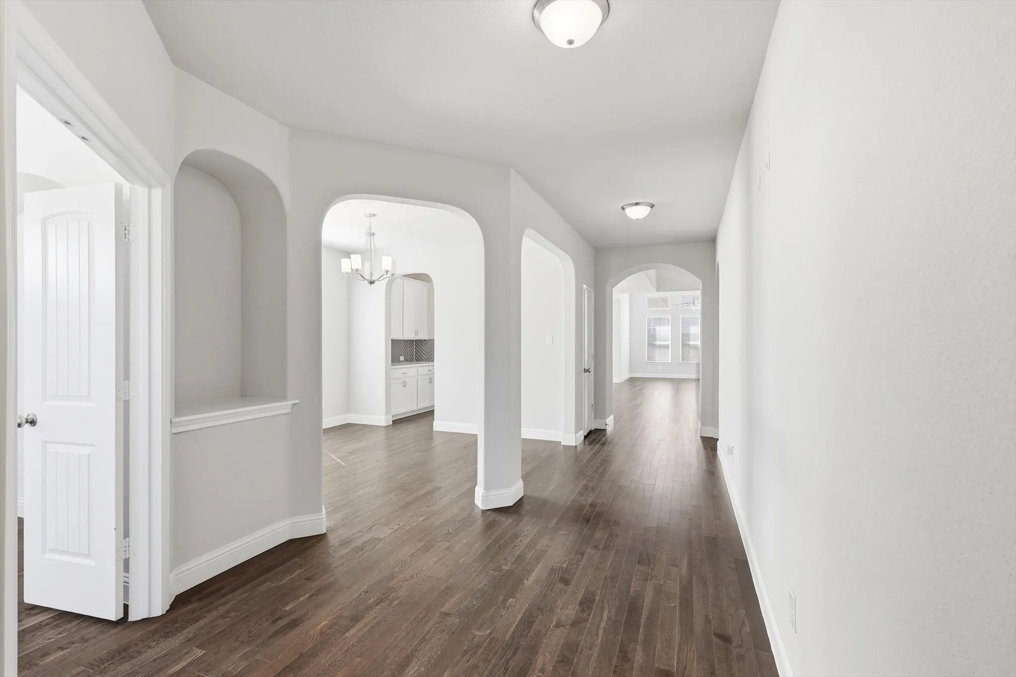 Long hallway featuring dark wood-finish flooring, multiple arched doorways, a built-in display nook, and flush-mount ceiling lighting